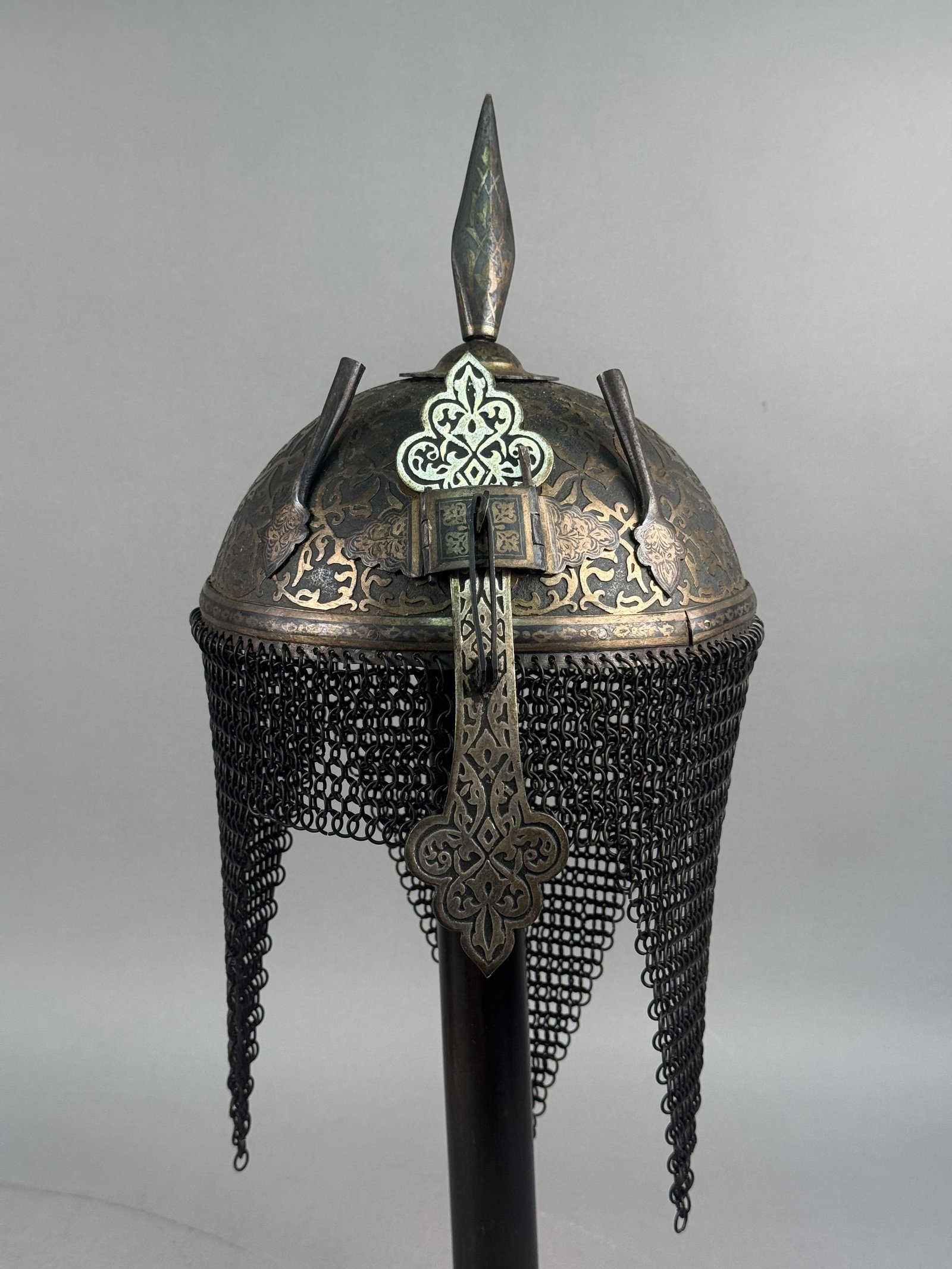 Indo-Persian Steel Kulah Khud Helmet: An Indo-Persian style steel helmet, commonly referred to as a kulah khud, featuring a hemispherical dome. The exterior of the bowl is extensively decorated with gold-toned metal overlay applied in a
