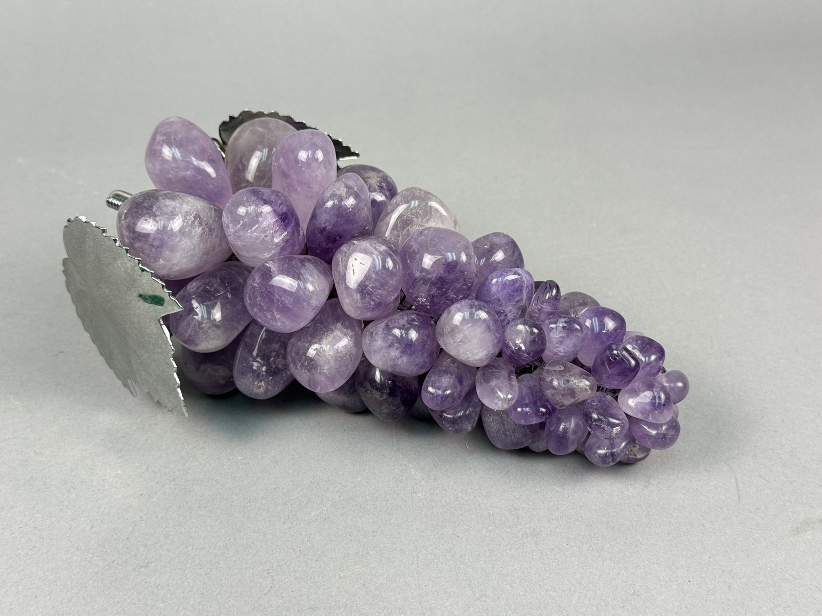 Mid-Century Style Amethyst Grape Cluster: A decorative grape cluster composed of numerous tumbled and polished amethyst stones in various shades of purple. Each individual stone is wired to a central metal armature to form a tapered bunch. Th