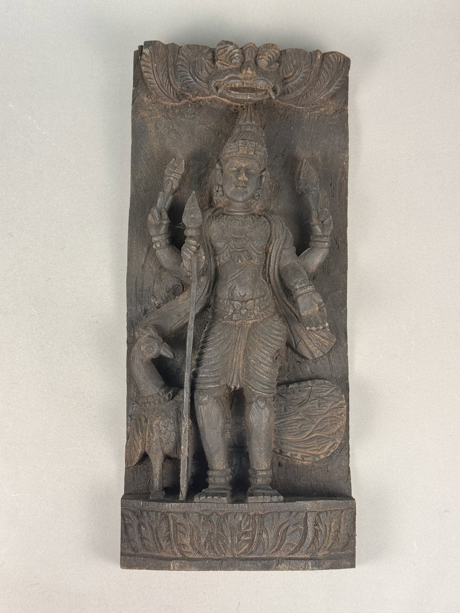South Indian Carved Wood Relief Panel: A carved dark hardwood relief panel, likely an architectural element from a South Indian temple chariot (rath) or doorway. The figure stands on a rectangular base decorated with foliate carvings. The 