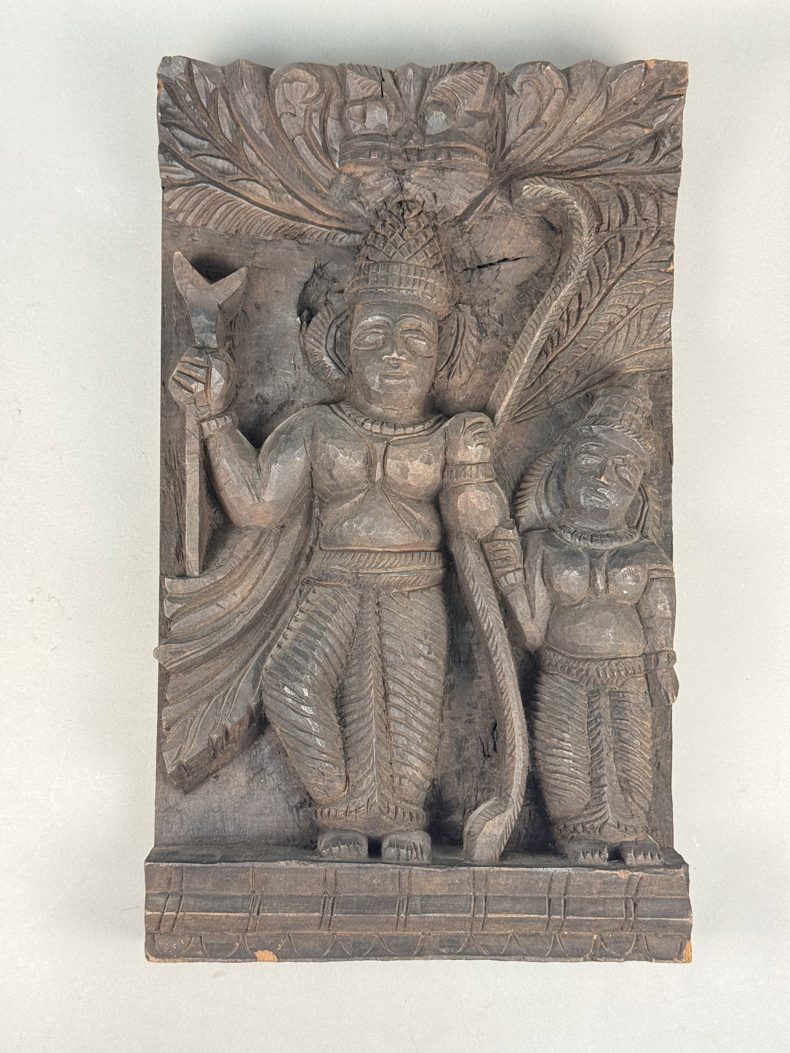 Indian Carved Hardwood Relief Panel: This hand-carved wood relief panel depicts a divine Hindu couple standing beneath a stylized foliage canopy, possibly representing a sacred tree. On the reverse, a partially preserved paper label is