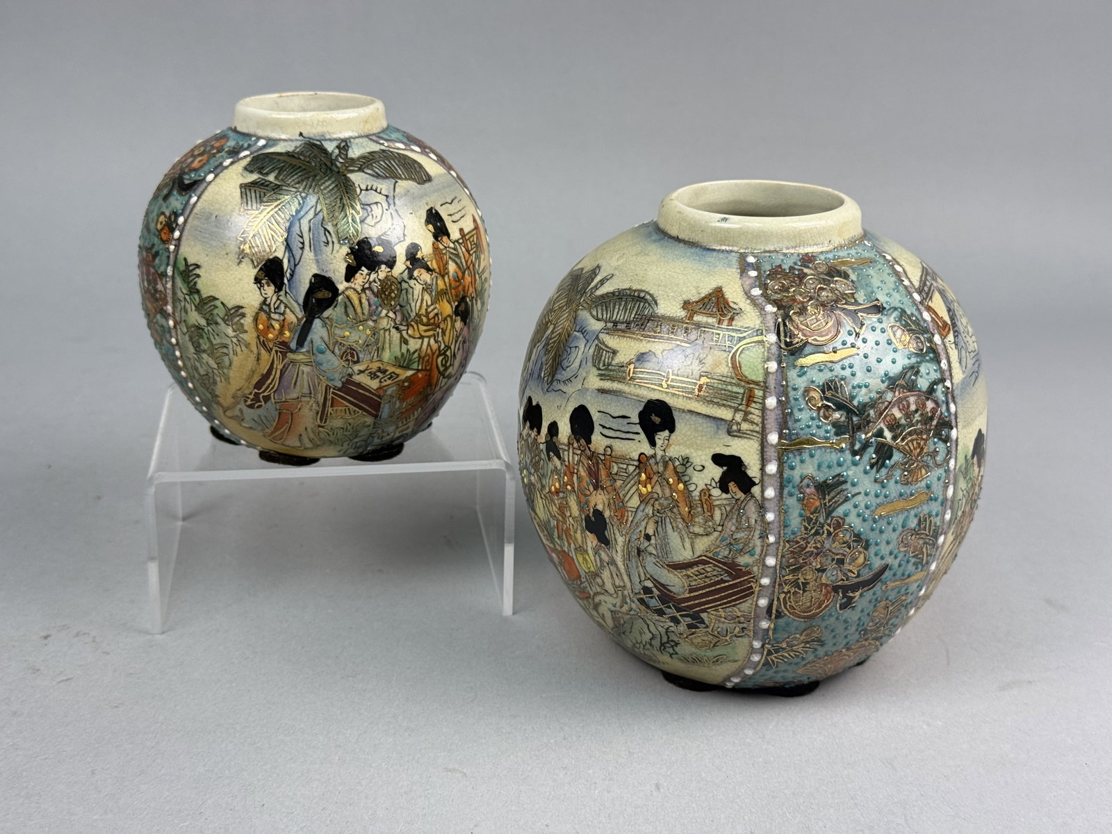 Graduated Japanese Satsuma Style Vases: A pair of graduated globular ceramic vases crafted from cream-colored earthenware with a fine crackle glaze. The vases are decorated in the Satsuma style with overglaze enamels, raised moriage