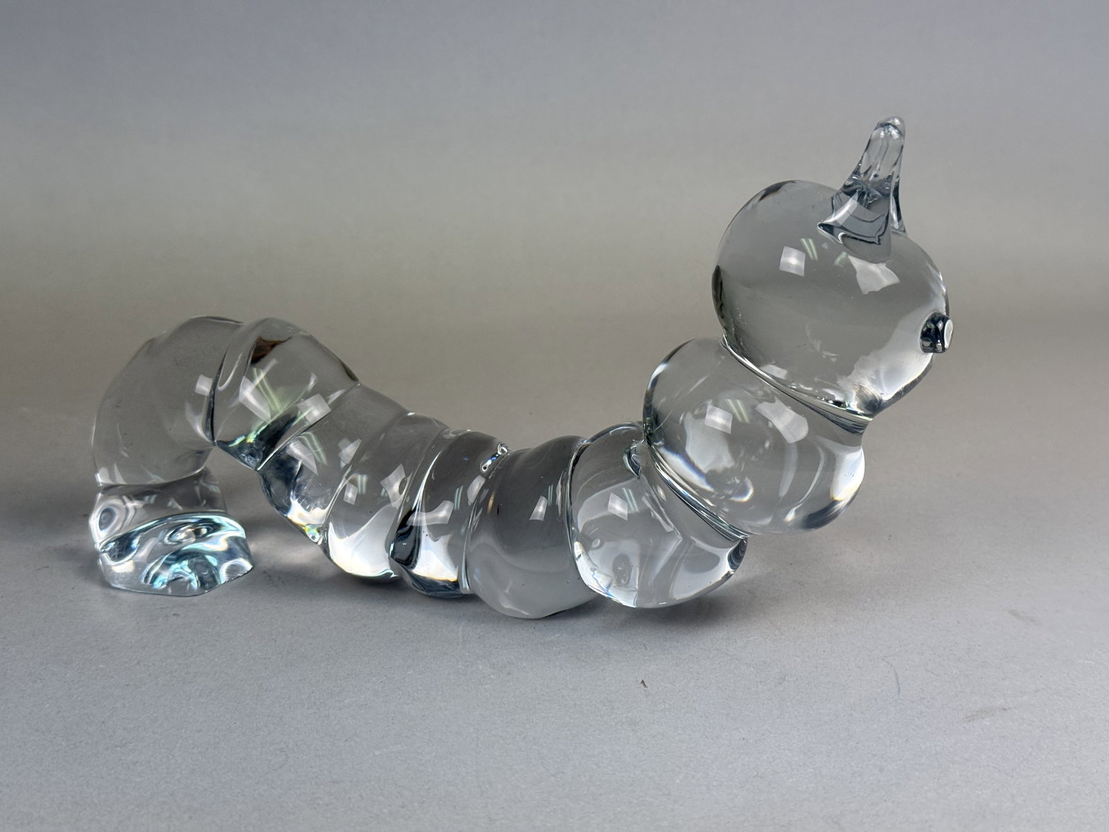 Signed Studio Glass Caterpillar Figurine: This is a solid clear studio glass figurine depicting a segmented caterpillar in an arched pose. The piece is constructed from heavy, clear glass with a series of rounded segments. The head features t