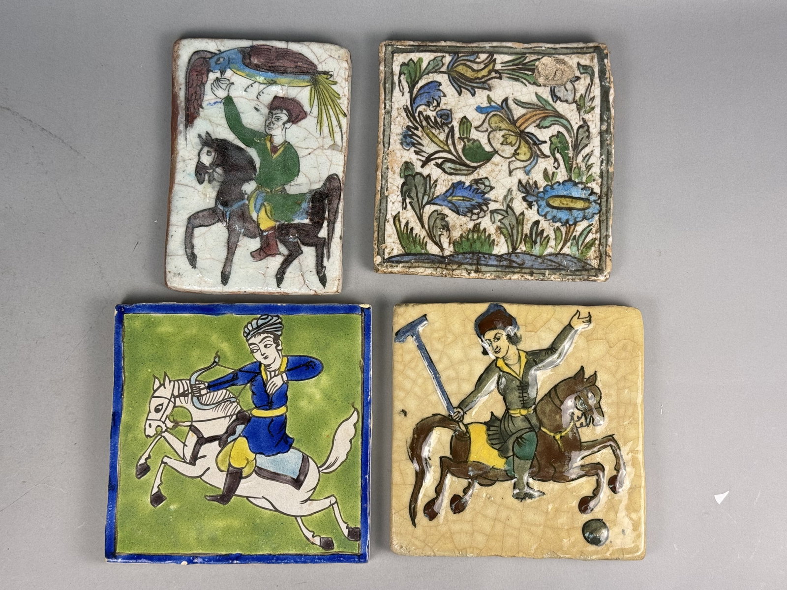 4 Persian Qajar Style Polychrome Earthenware Tiles: This set of four hand-painted ceramic tiles is executed in the Persian Qajar style, featuring traditional courtly pastimes and floral motifs. The grouping includes one rectangular tile and three squar