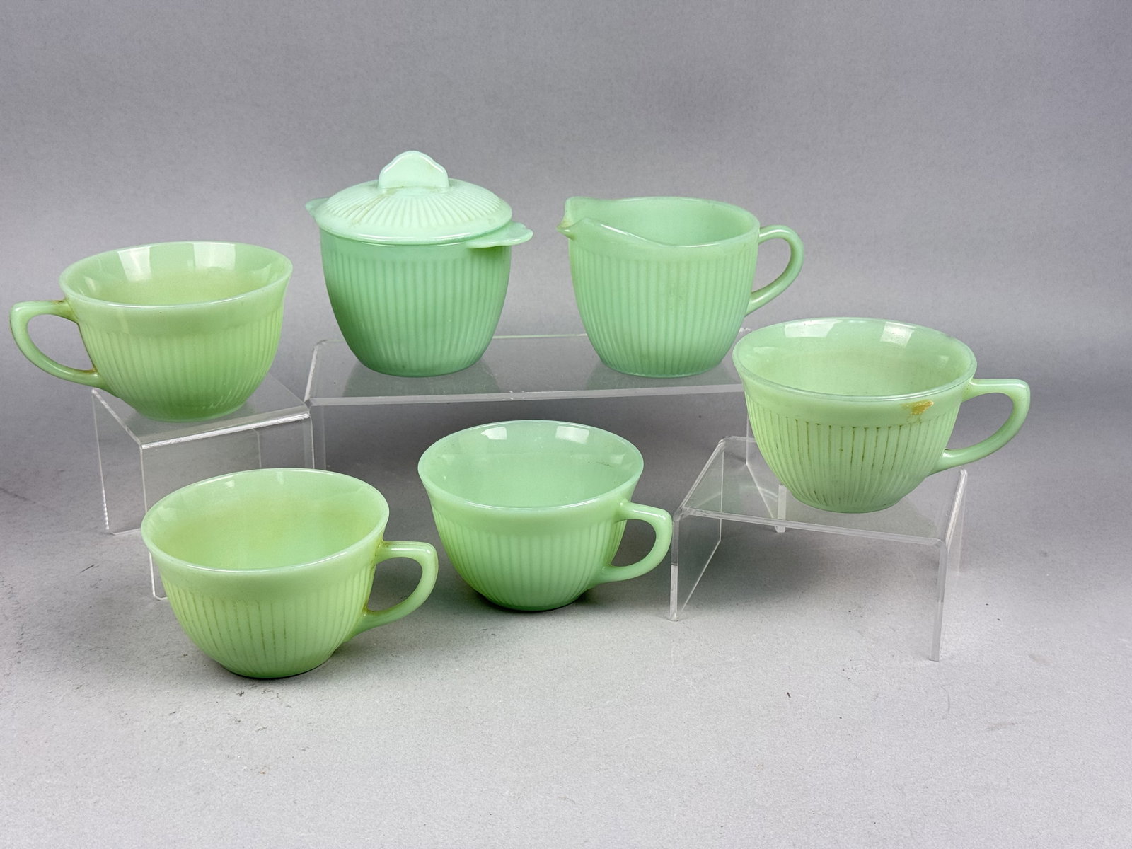 Fire-King Jane Ray Jadeite Glass Tableware: The collection consists of four cups, one creamer, one lidded sugar bowl and six saucers. Each piece is made from jadeite, an opaque light green milk glass. The Jane Ray design is characterized by ver