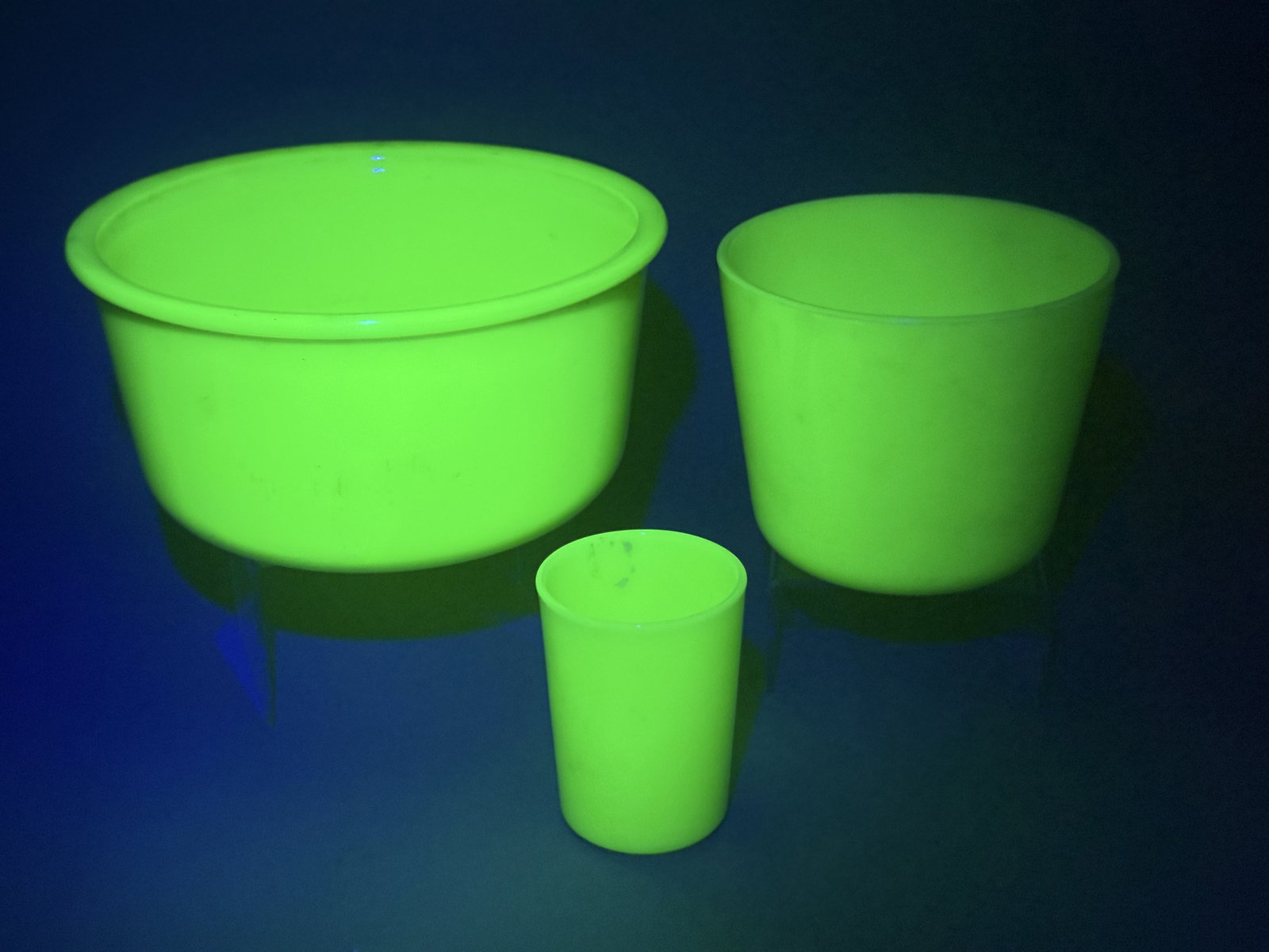 A Trio of Jadeite Uranium Glass Kitchenware: A trio of vintage jadeite green kitchenware pieces, including a large wide-rimmed mixing bowl, a medium cylindrical canister or refrigerator dish, and a small tumbler or custard cup. These items are c