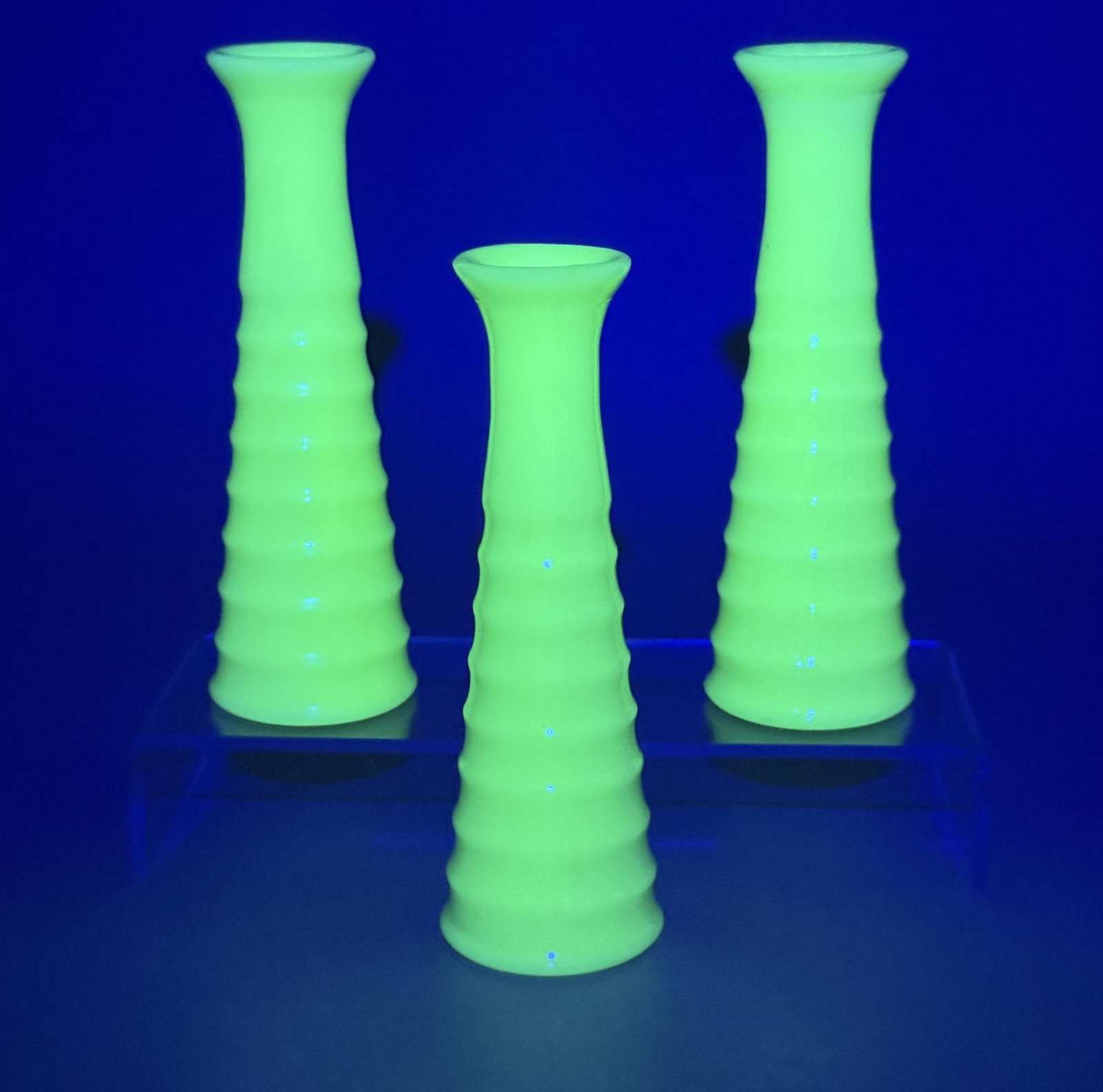 Jadeite Uranium Glass Beehive Bud Vases: A trio of small bud vases crafted from opaque mint green uranium glass, commonly known as jadeite. These pieces feature a tapered conical form with horizontal ribbing, often referred to as a beehive