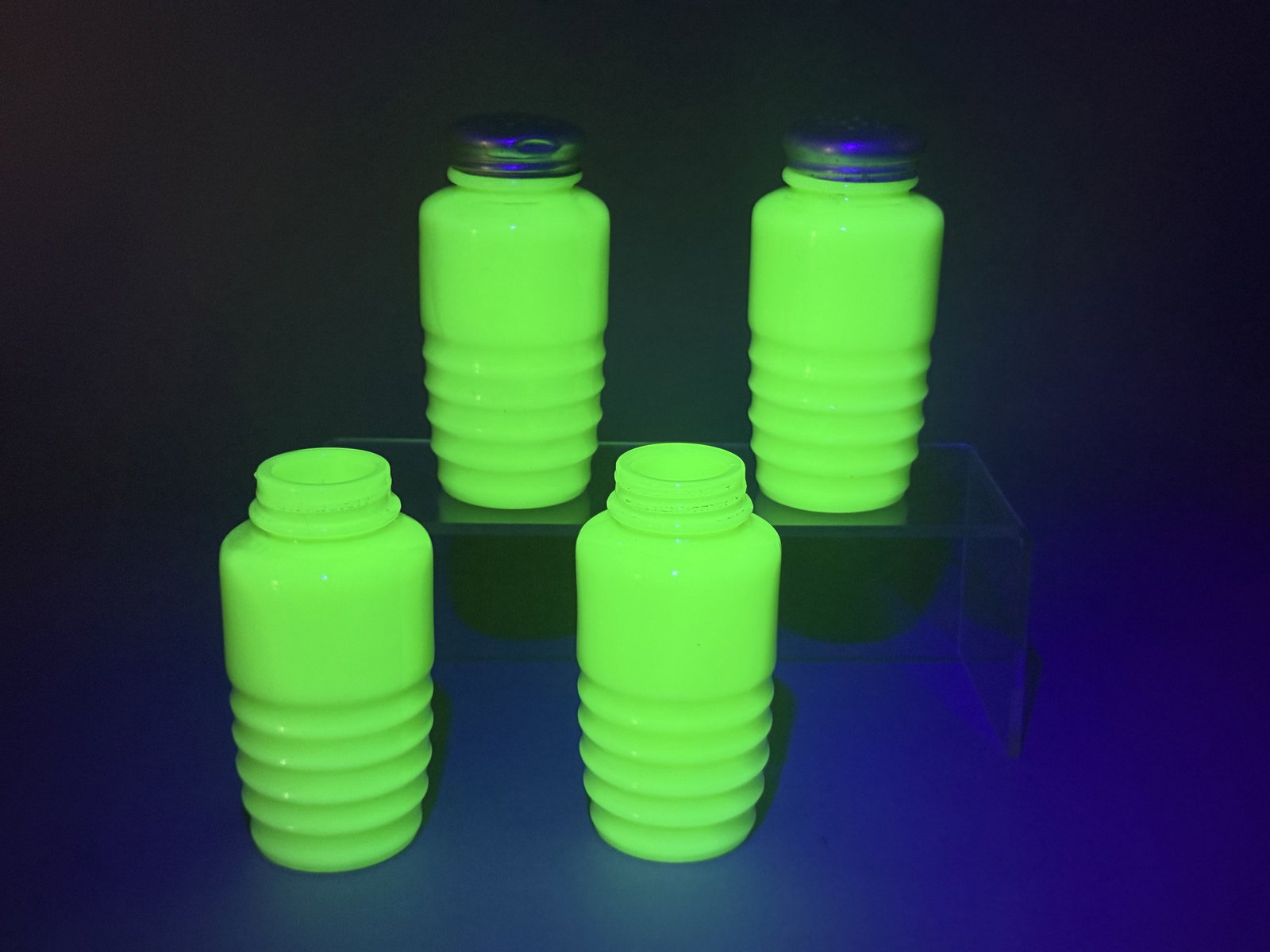 Four Uranium Jadeite Glass Beehive Shakers: This group of kitchenware shakers is crafted from opaque jadeite green milk glass, attributed to the Jeannette Glass Company. Each shaker has a smooth, rounded shoulder tapering to a threaded neck.