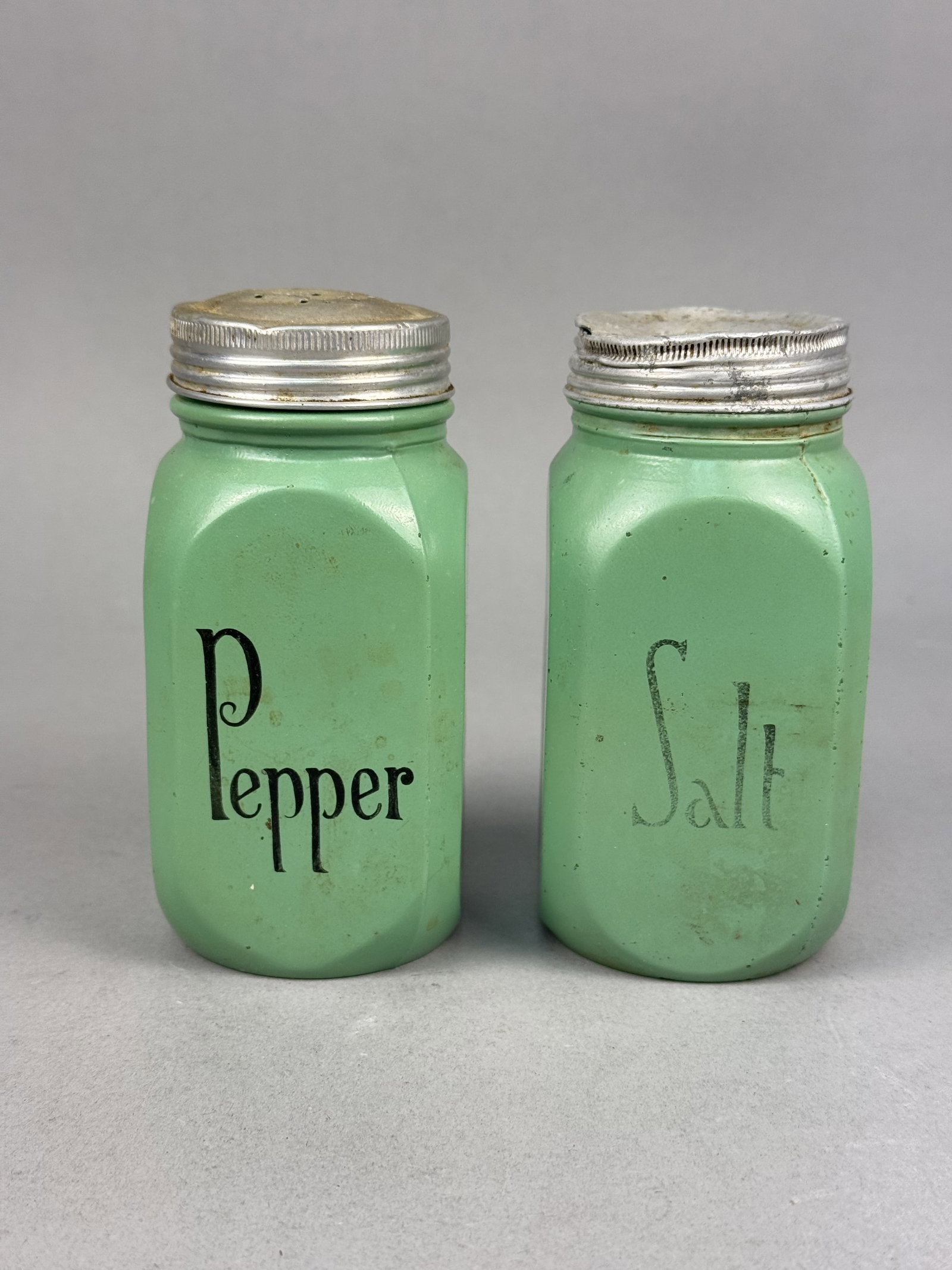 Jadeite Glass Arched Range Salt & Pepper Shakers: A pair of vintage American range-sized salt and pepper shakers crafted from opaque jadeite green glass. Each shaker features a square form with four recessed arched side panels. Items of this form