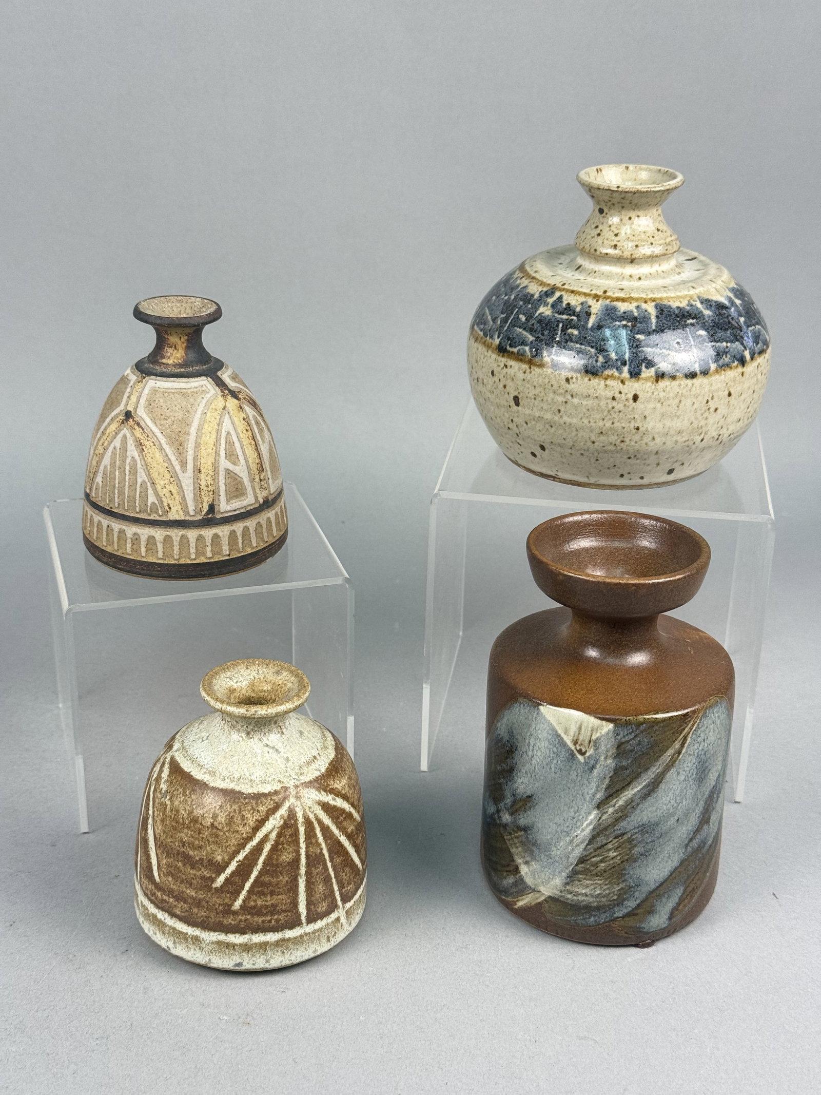 Mid-Century American Studio Pottery Bud Vases: A collection of multiple mid-century modern stoneware bud vases featuring varied glaze techniques and forms. The assortment includes one cylindrical vase with a matte brown ground and a glossy abstrac