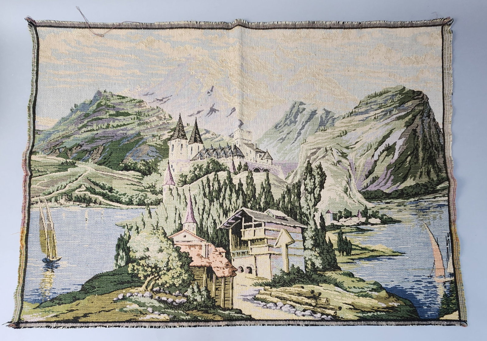 Belgian Machine-Woven Tapestry: A machine-woven pictorial tapestry featuring a romanticized European landscape scene. The edges of the textile are unfinished. 34 inches x 25 inches. The item is in overall good condition. Minor frayi