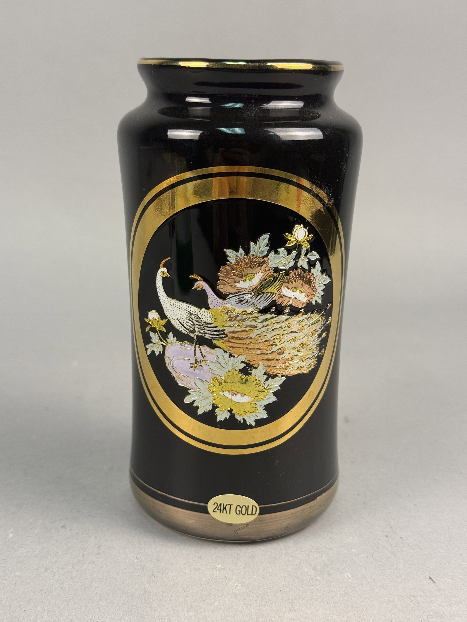 Japanese Black Porcelain Vase with Peacock: This Japanese cylindrical porcelain vase features a high-gloss black glaze and a central oval medallion executed in the Art of Chokin style. The medallion depicts a pair of peacocks among floral bloss