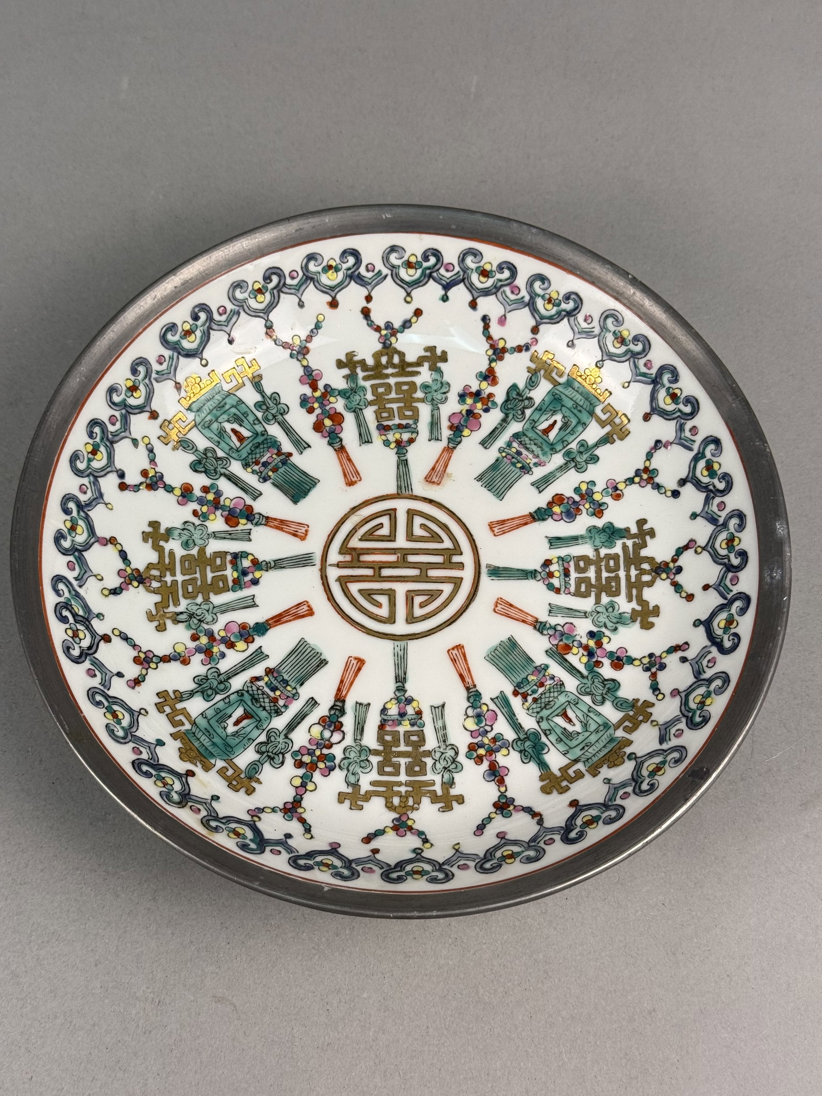 Mid-Century Pewter-Encased Japanese Porcelain Plate: A circular porcelain plate mounted within a dark gray pewter casing. The interior white porcelain surface features hand-painted overglaze polychrome enamel decoration including shades of green, iron-r