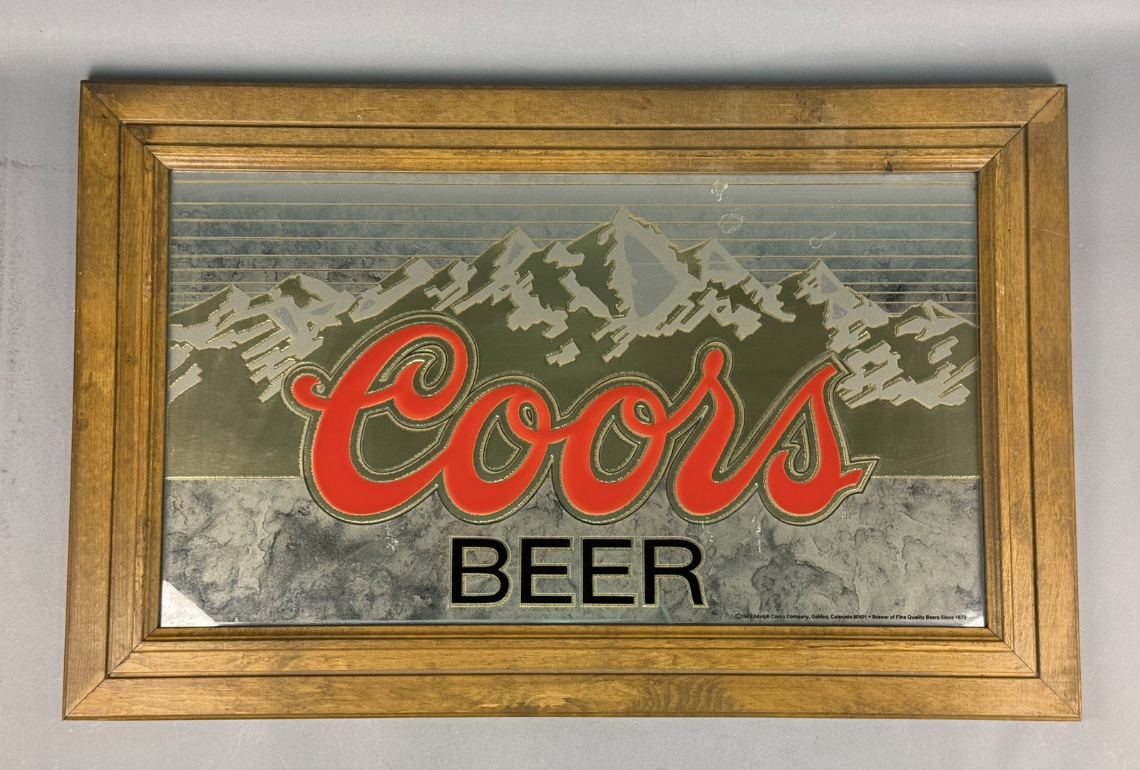 1988 Coors Beer Framed Bar Mirror: This vintage advertising mirror was produced for the Adolph Coors Company by Signs & Glassworks Inc. The mirror features the Coors script logo in red with a silver and black double outline positioned 