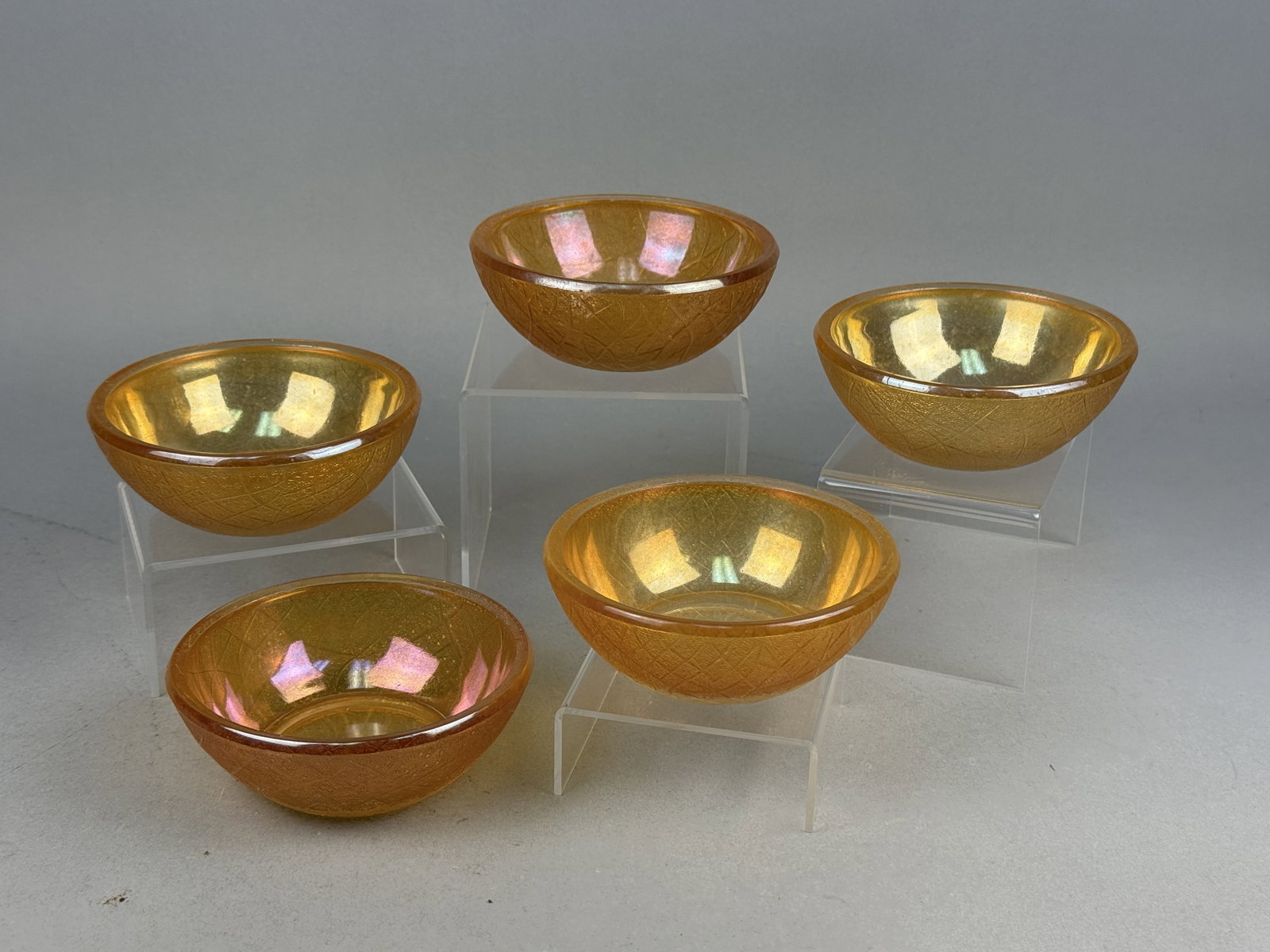 Marigold Carnival Glass Iridescent Bowls: A set of pressed glass bowls featuring a marigold iridescent finish over an amber-toned base. The exterior of each piece is decorated with a textured pattern consisting of a stippled background overla