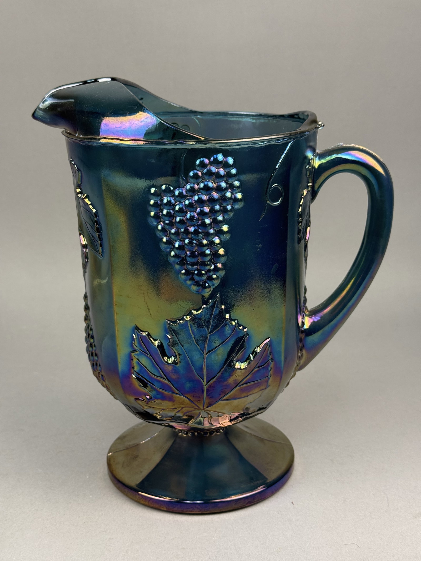 Indiana Glass Harvest Grape Carnival Glass Pitcher: This footed pitcher is an example of the Harvest Grape pattern produced by the Indiana Glass Company, which was frequently marketed under the Colony brand name. The vessel is crafted from pressed glas