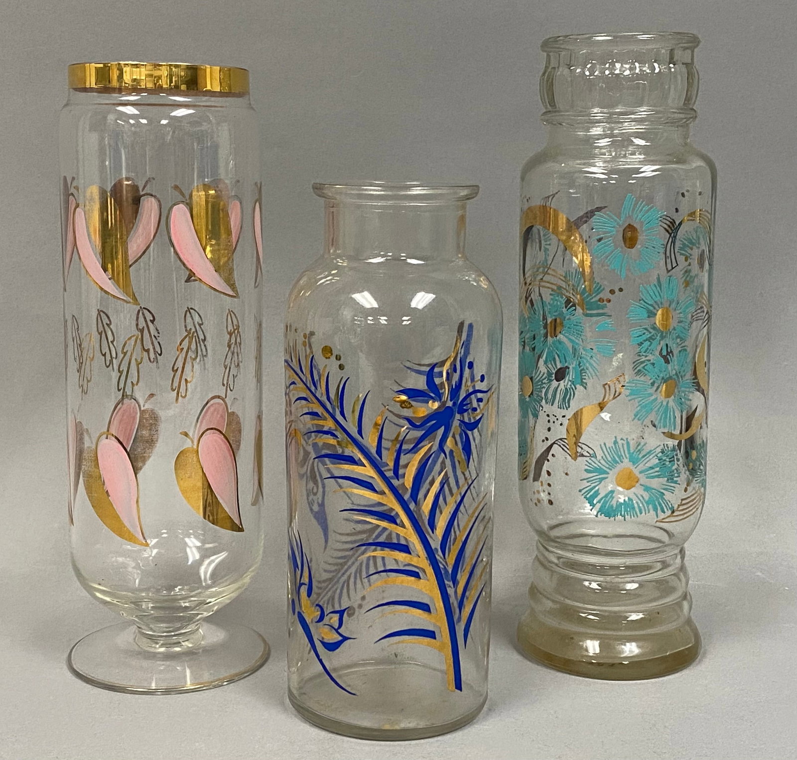 3 MCM Painted and Gilt Clear Glass Vases: This collection consists of three mid-century modern clear glass vases featuring hand-painted enameled and gilt decorations. The first vase is a footed cylindrical vessel decorated with two rows of he