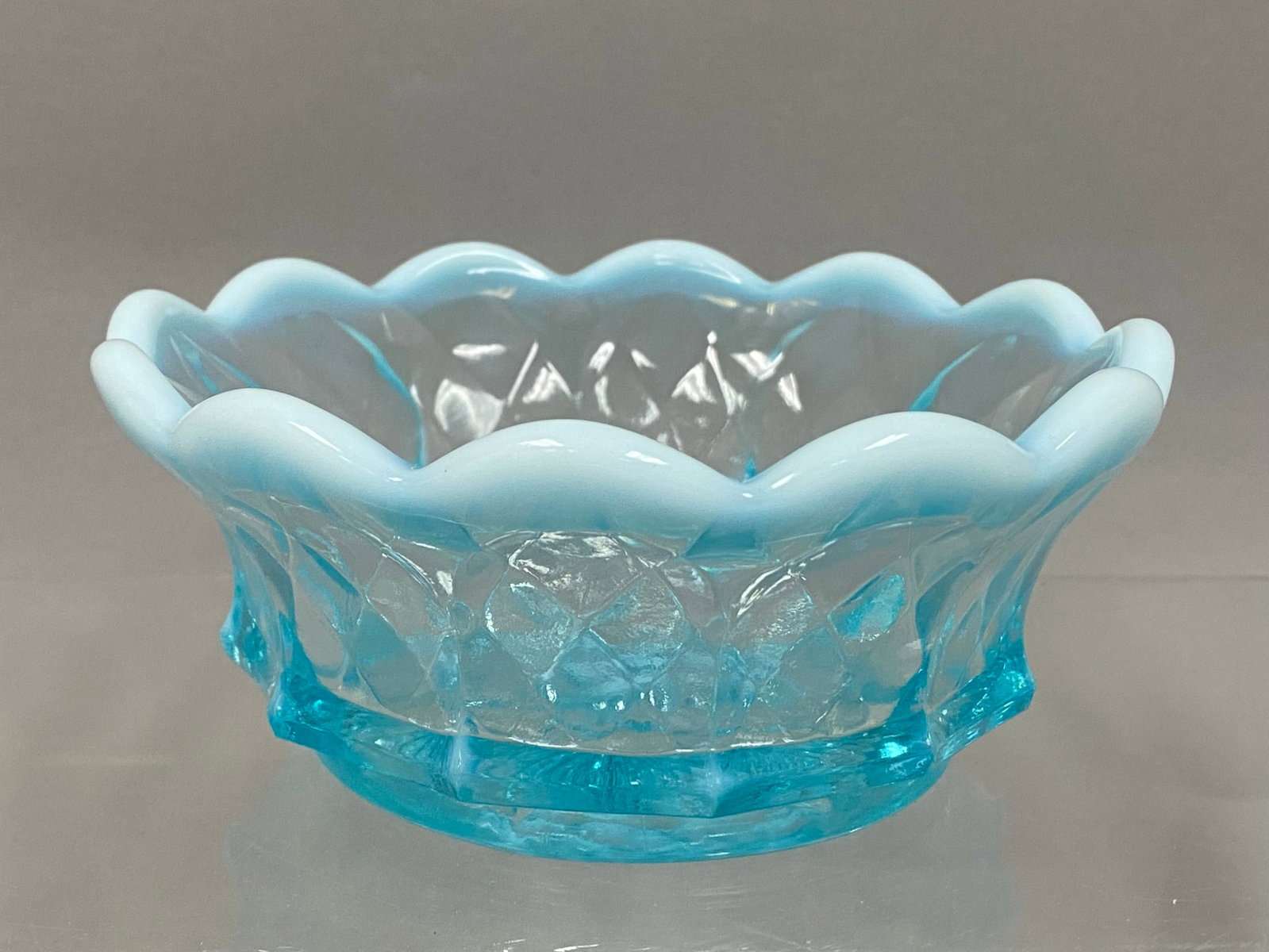 Fenton Blue Opalescent Diamond Quilt Glass Bowl: This blue opalescent glass bowl was produced by the Fenton Art Glass Company. The piece features a translucent light blue body with a milky white opalescent finish on the crimped, scalloped rim. The