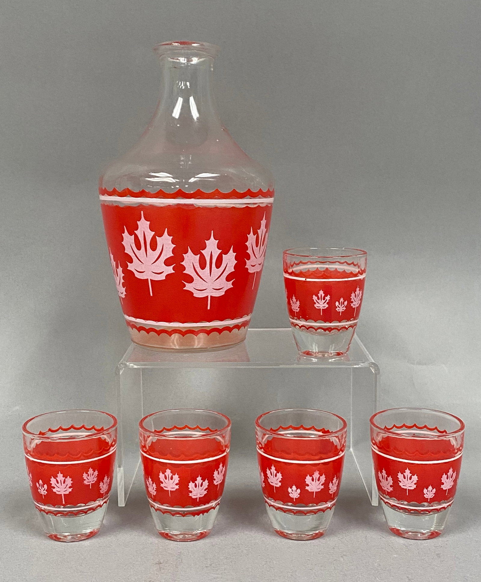 6-Piece Set of French Vintage Glassware: This vintage 6-piece glass beverage set consists of one decanter and 5 matching shot glasses. Each piece is crafted from clear glass and features a mid-century modern design with a fired-on red band. 
