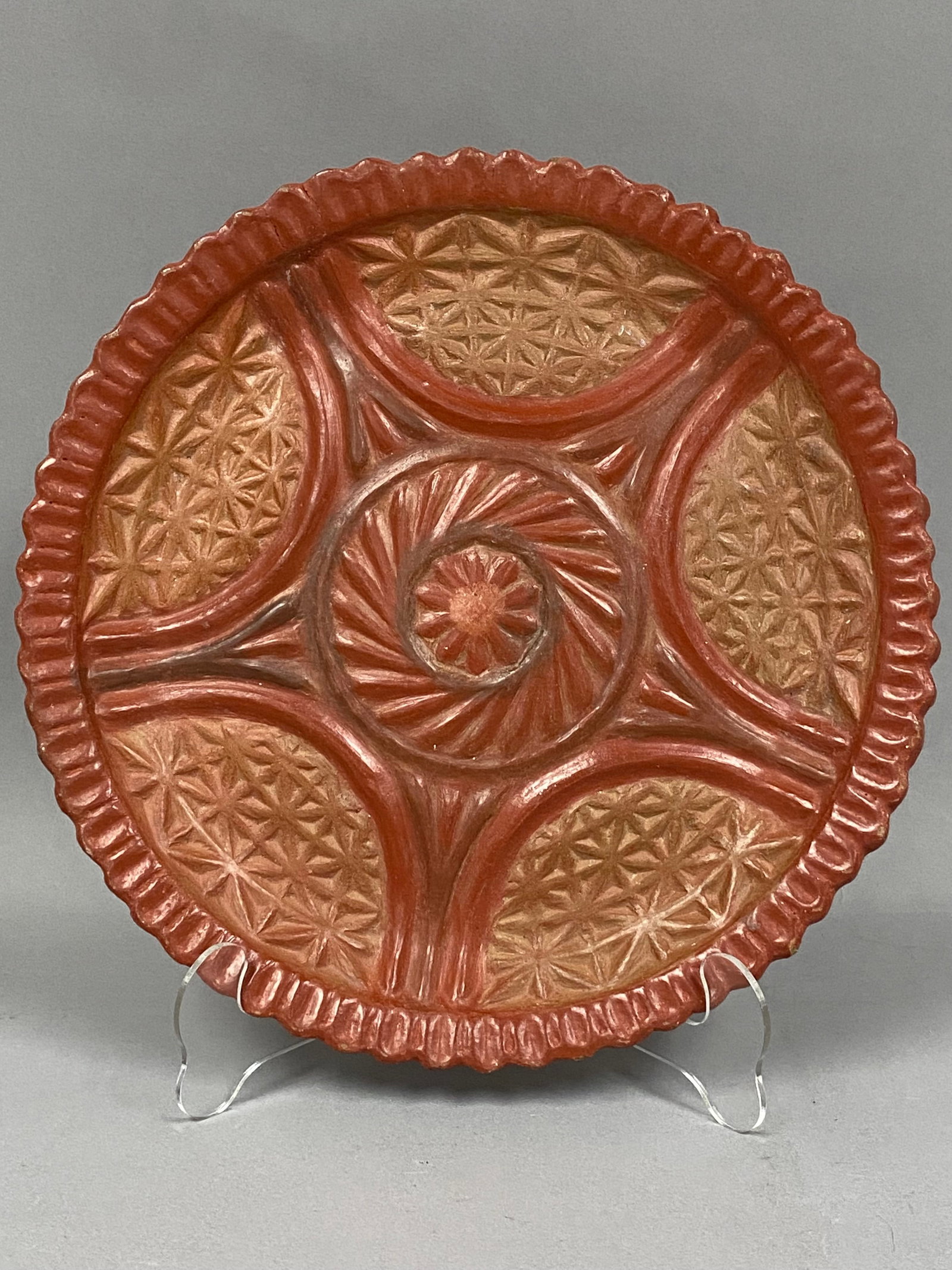 Earthenware Wall Charger: A circular, hand-finished earthenware wall charger crafted from buff-colored clay. The front of the piece is decorated with high-relief carved or molded geometric and stylized floral motifs. A central