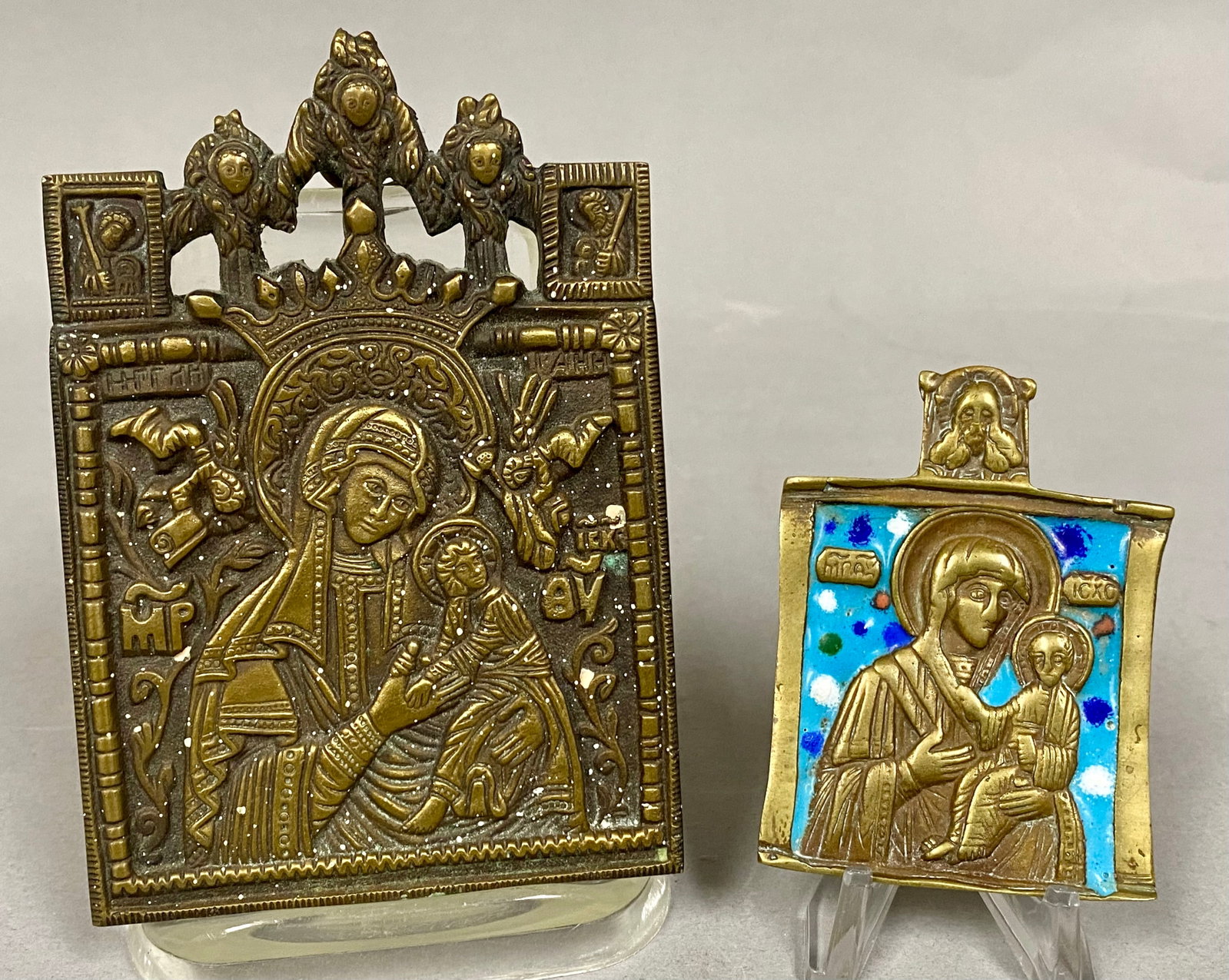 2 Russian Orthodox Cast Brass Travel Icons: This lot consists of two Russian Orthodox cast brass travel icons (plaquettes) dating to the 19th century. The larger icon depicts the Mother of God Strastnaya (Our Lady of the Passion). The central