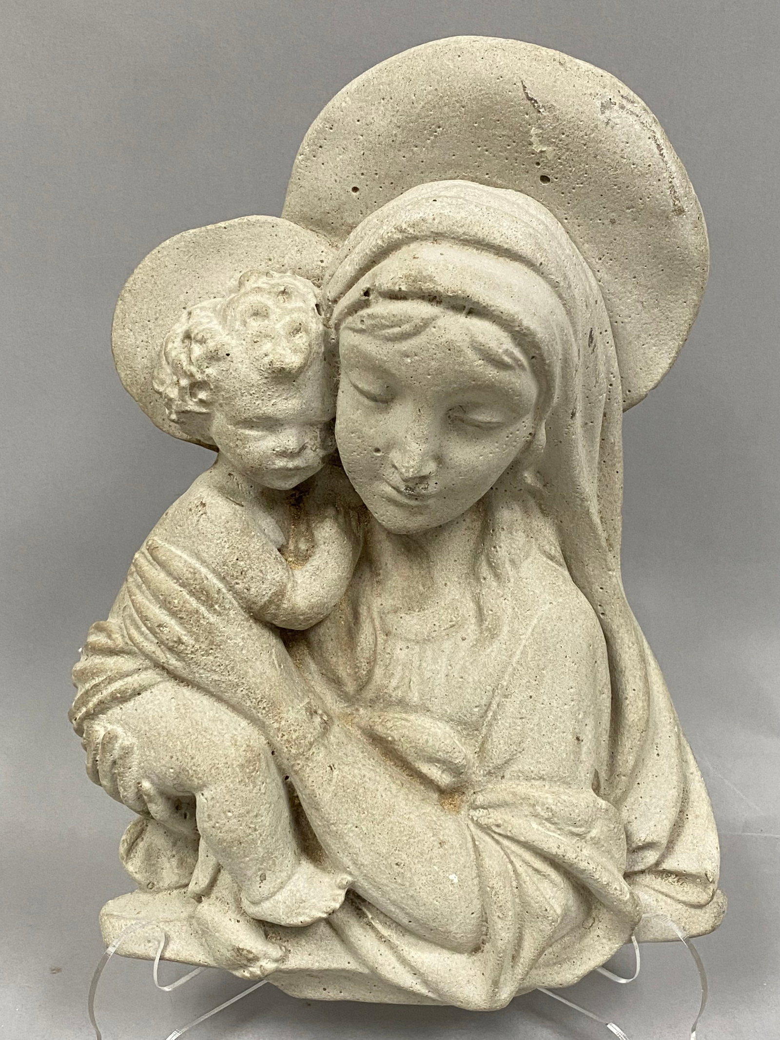 Cast Stone Plaque of the Madonna and Child: This religious wall plaque features a high-relief sculpture depicting the Virgin Mary cradling the infant Jesus. Both figures are presented with circular halos. The Madonna is shown in a