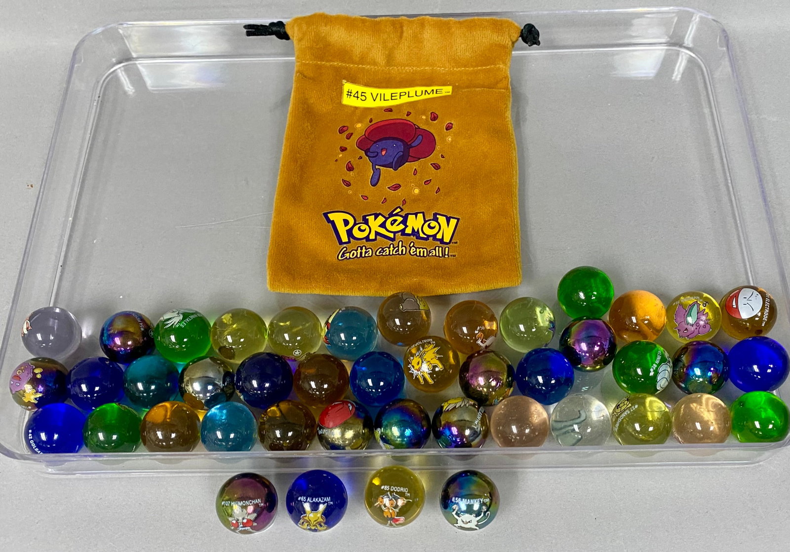 44 Pok?©mon Marbles & Vileplume Pouch: This lot features 44 marbles and a character-themed storage bag produced by Toy Biz under official license from Nintendo, Creatures, and Game Freak, dating to approximately 2000. The collection consis
