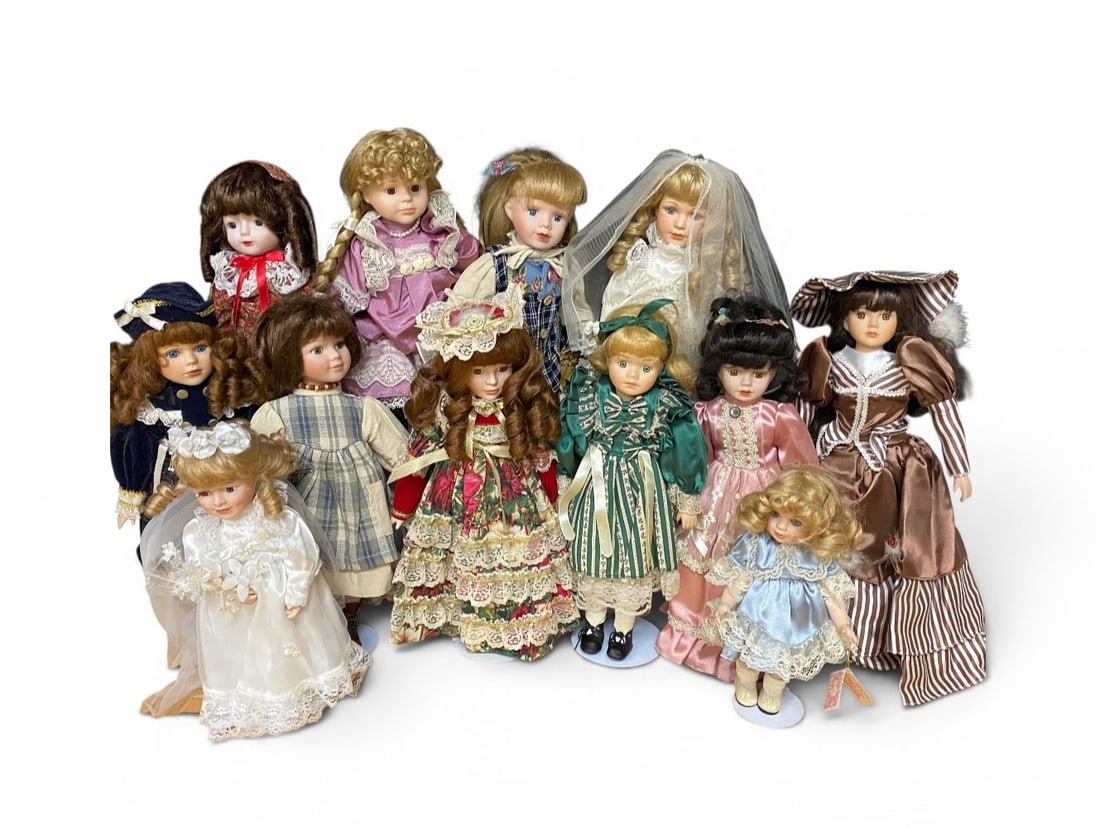 12 Contemporary Collectible Porcelain Dolls: This lot consists of a collection of 12 contemporary collectible dolls featuring porcelain components and cloth bodies. The dolls are constructed with bisque-style porcelain heads, forearms, and lower