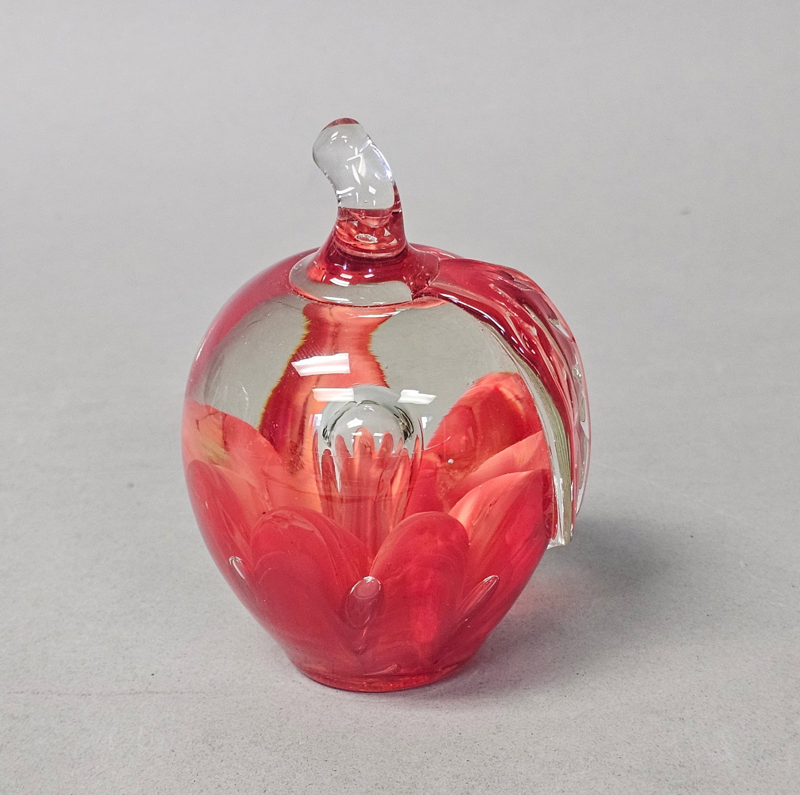 Joe St. Clair Glass Apple Paperweight: This hand-blown art glass paperweight by Joe St. Clair is crafted in the form of an apple with a vibrant red interior core. The central design features pulled petal forms and controlled bubbles encase