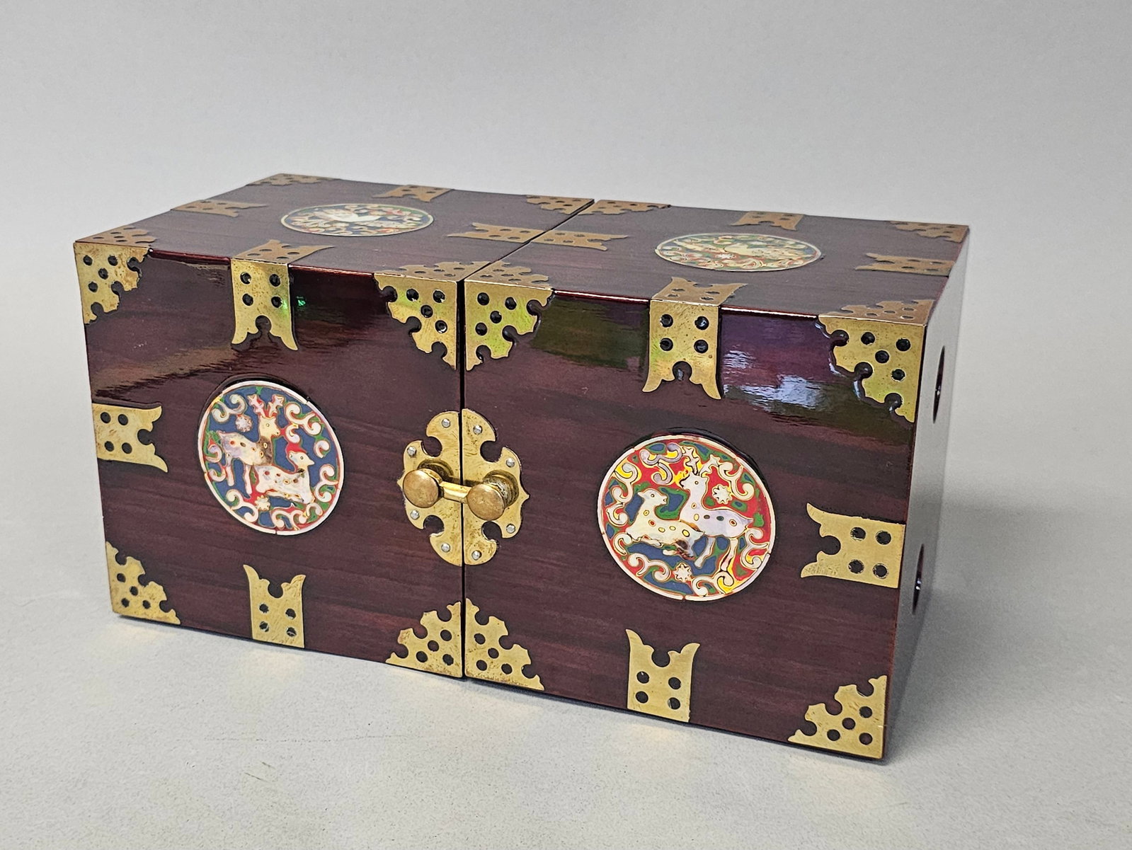Korean Lacquered Folding Jewelry Chest: This split-case decorative chest is constructed from dark lacquered hardwood accented with ornate perforated brass hardware and corner plates. The exterior is embellished with four circular cloisonne 