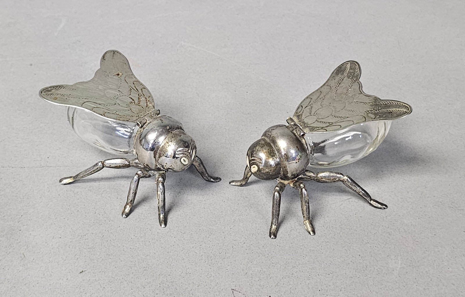 Silver Plated Fly Salt & Pepper Shakers: A pair of silver plated and glass salt and pepper shakers modeled in the naturalistic form of flies. Each insect features a clear glass abdomen with a threaded neck that attaches to a silver head and 
