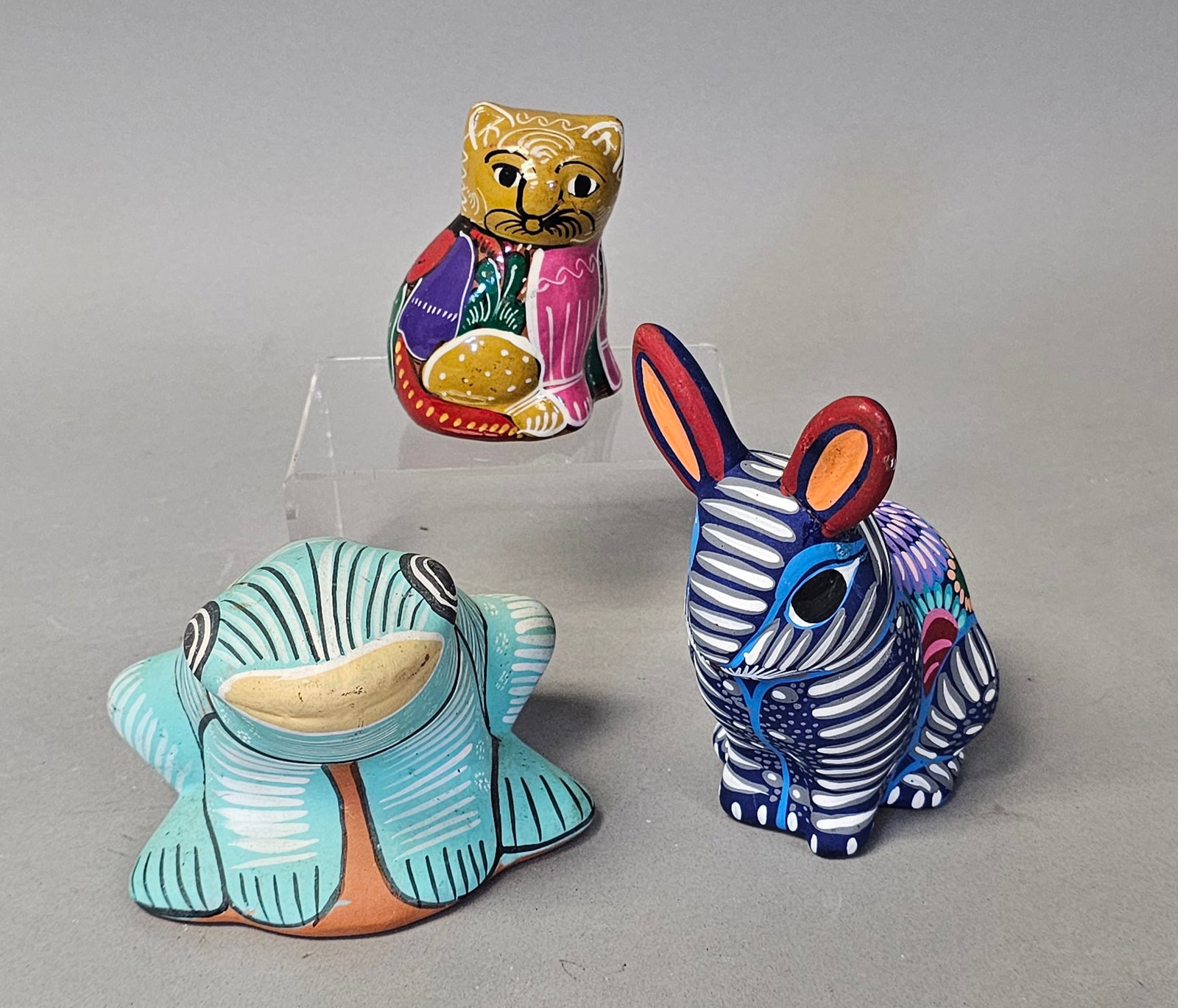 Three Mexican Ceramic Animal Figurines: A trio of hand-painted terracotta figurines comprising a frog, a cat, and a rabbit decorated in vibrant Mexican folk art motifs. The frog is dated 1992 and features teal linear patterns, while the cat
