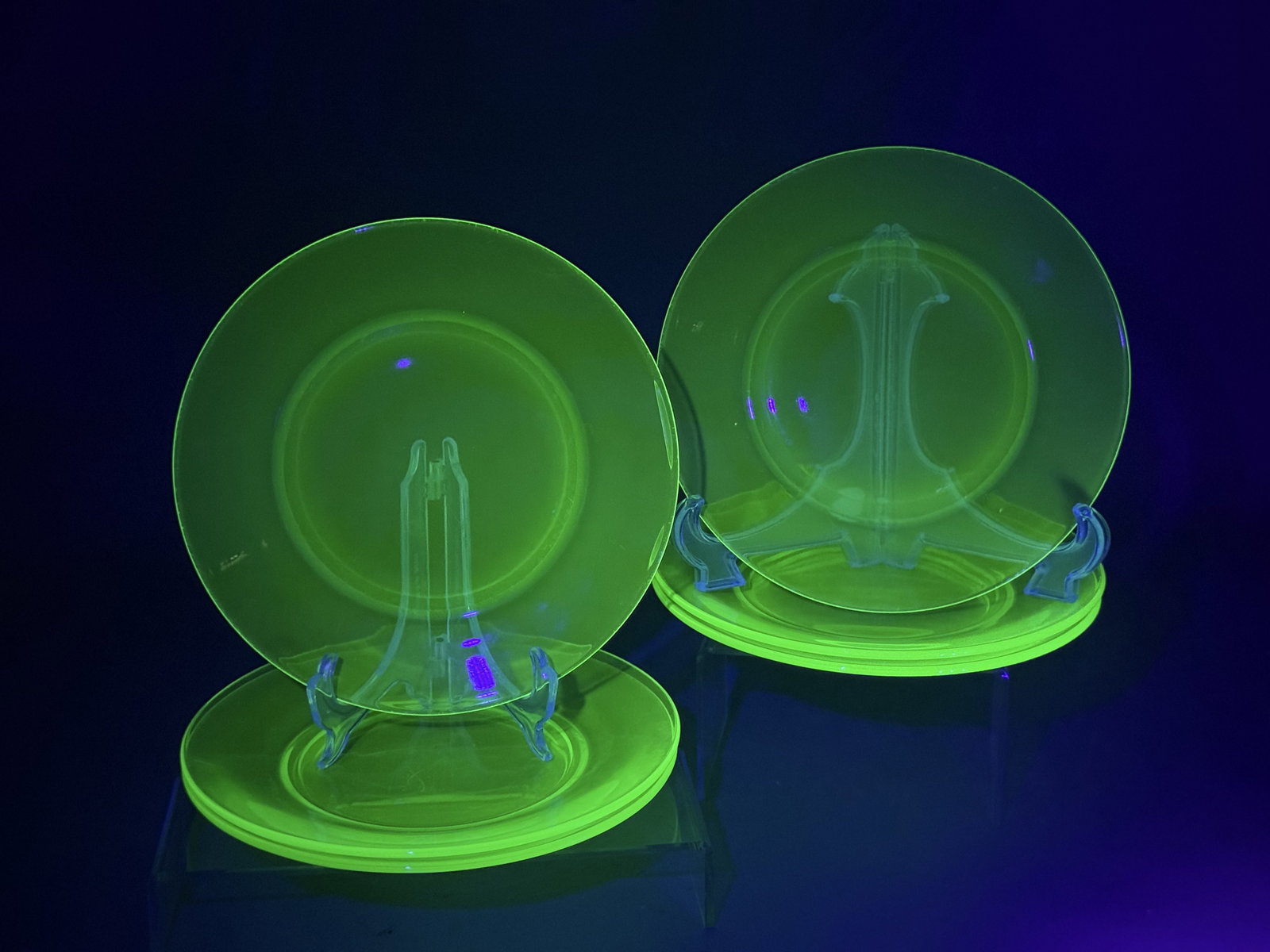 Six Green Uranium Glass Plates: A set of six seafoam green uranium glass plates featuring a circular form with a wide rim and recessed center. Each piece is constructed from pressed glass without pontil marks and exhibits a bright