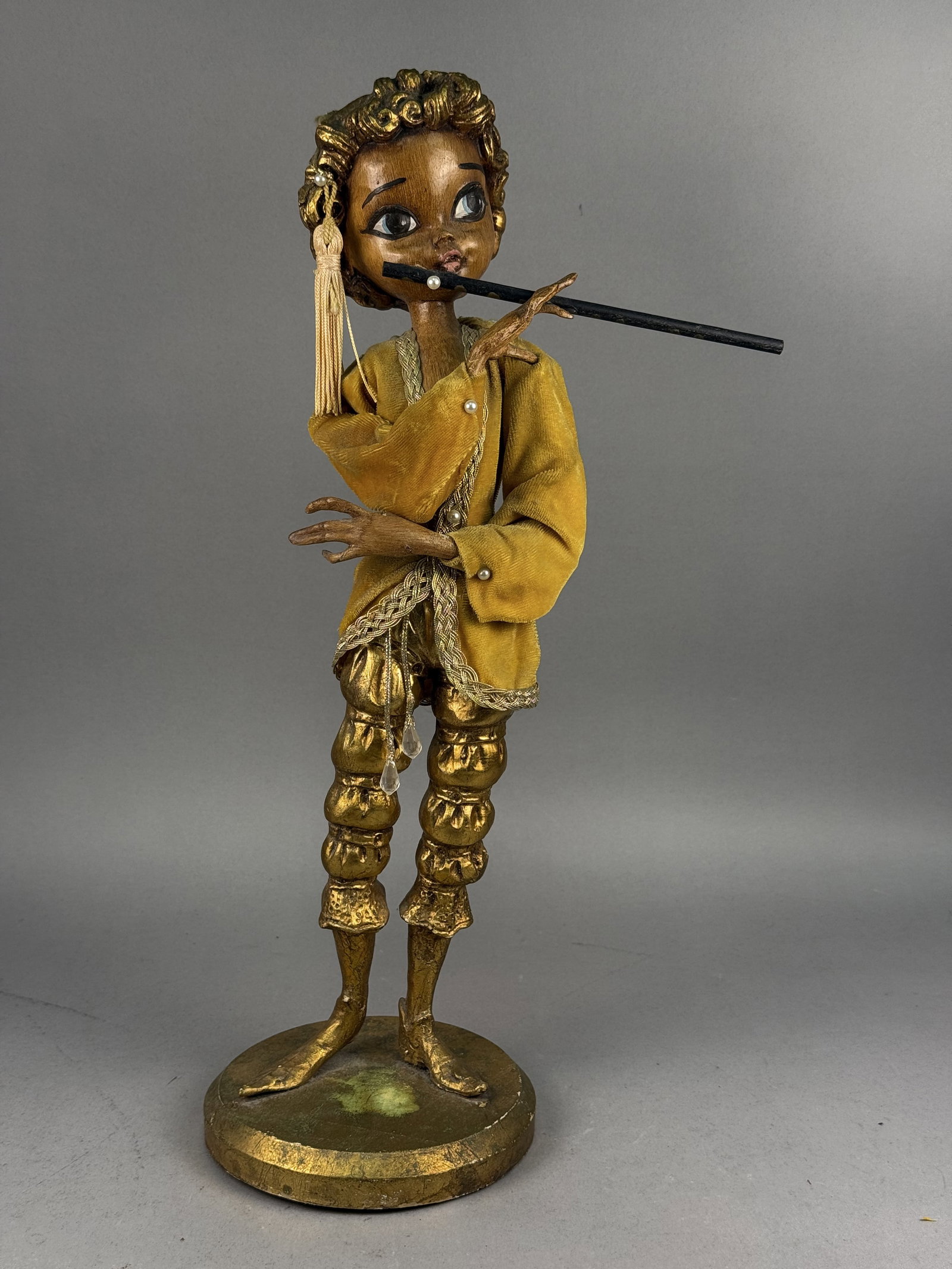 Mid-Century Stylized Musician Flutist Doll: This mid-century stylized composition doll depicts a courtly musician playing a flute. The figure features a faux bois wood-grain texture on the head, hands, and lower legs, complemented by