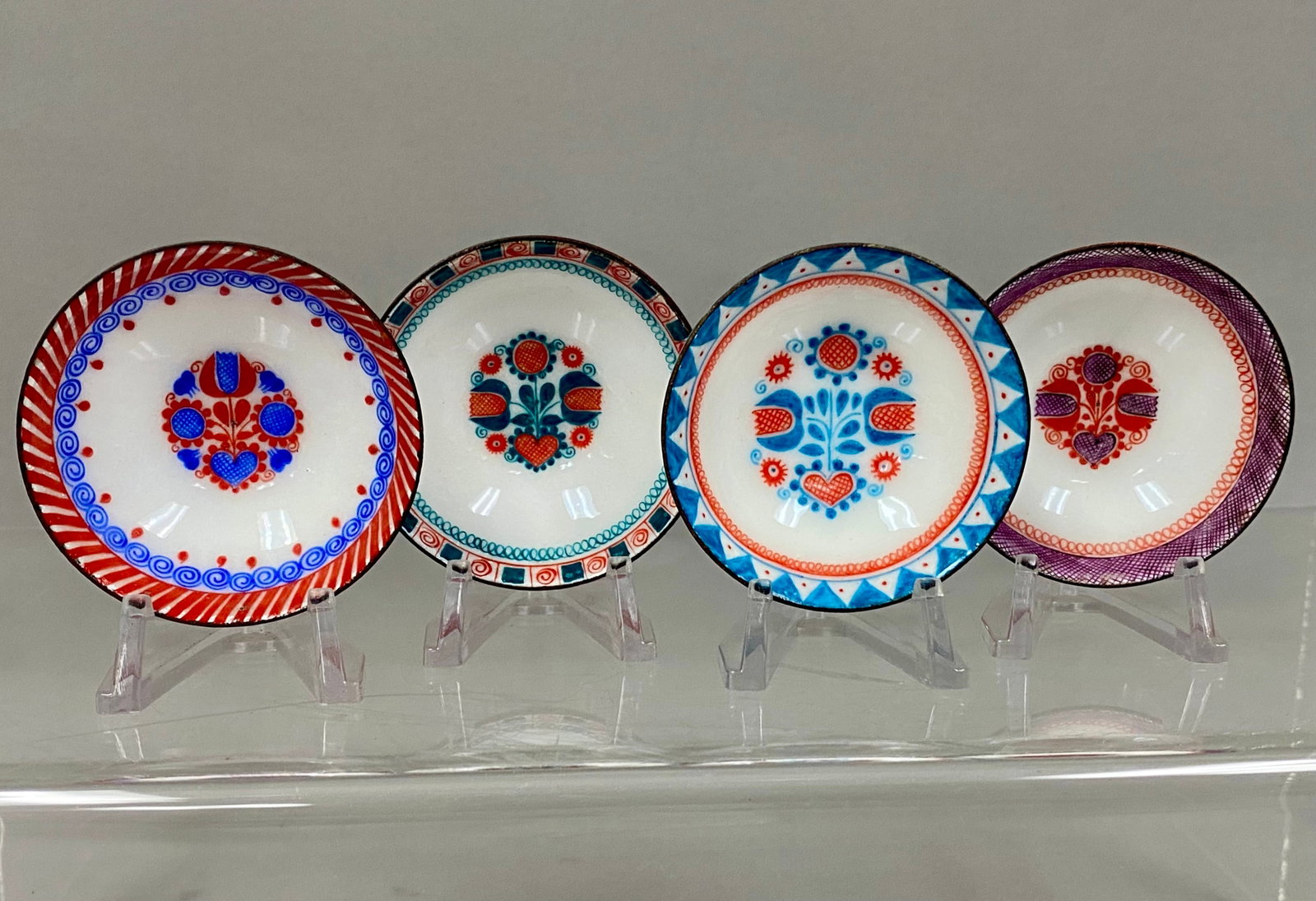 Steinbeck Austrian Enamel Dishes: This set of four hand-painted enamel on metal bowls was manufactured by Steinbeck Each piece displays central floral and heart folk art motifs surrounded by unique colorful borders on a white ground. 