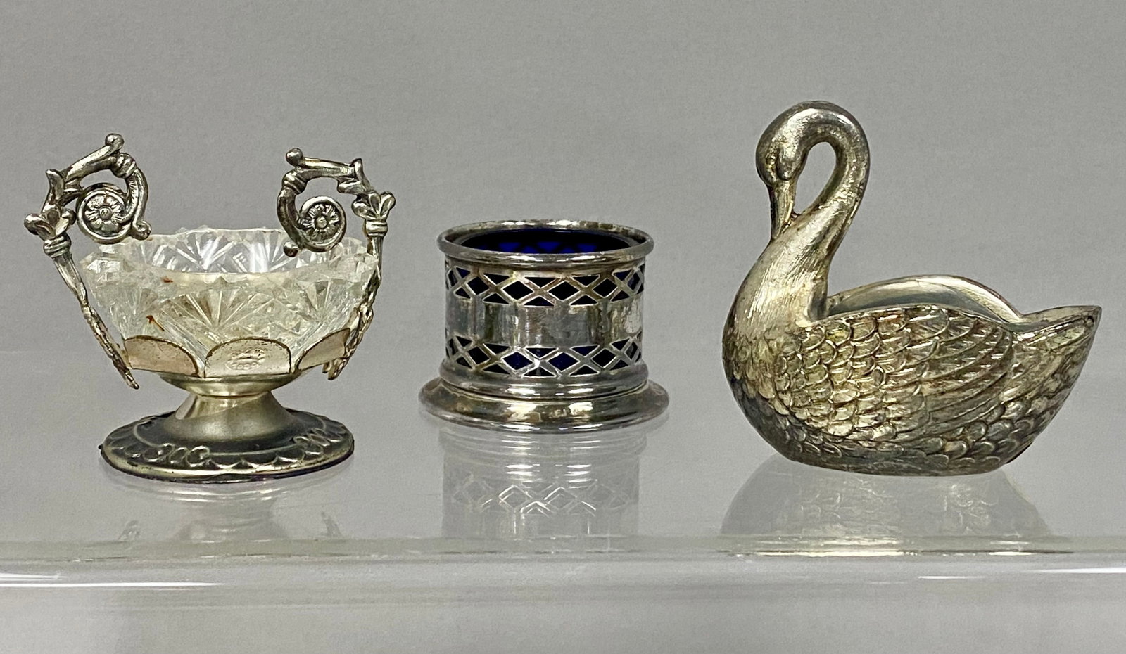 Three Vintage Silver-Plated Salt Cellars: This collection includes three assorted silver-plated salt cellars, each accompanied by glass or plastic liner. The group features a Rococo-style footed cellar marked ARGENT 1000, a cylindrical openwo