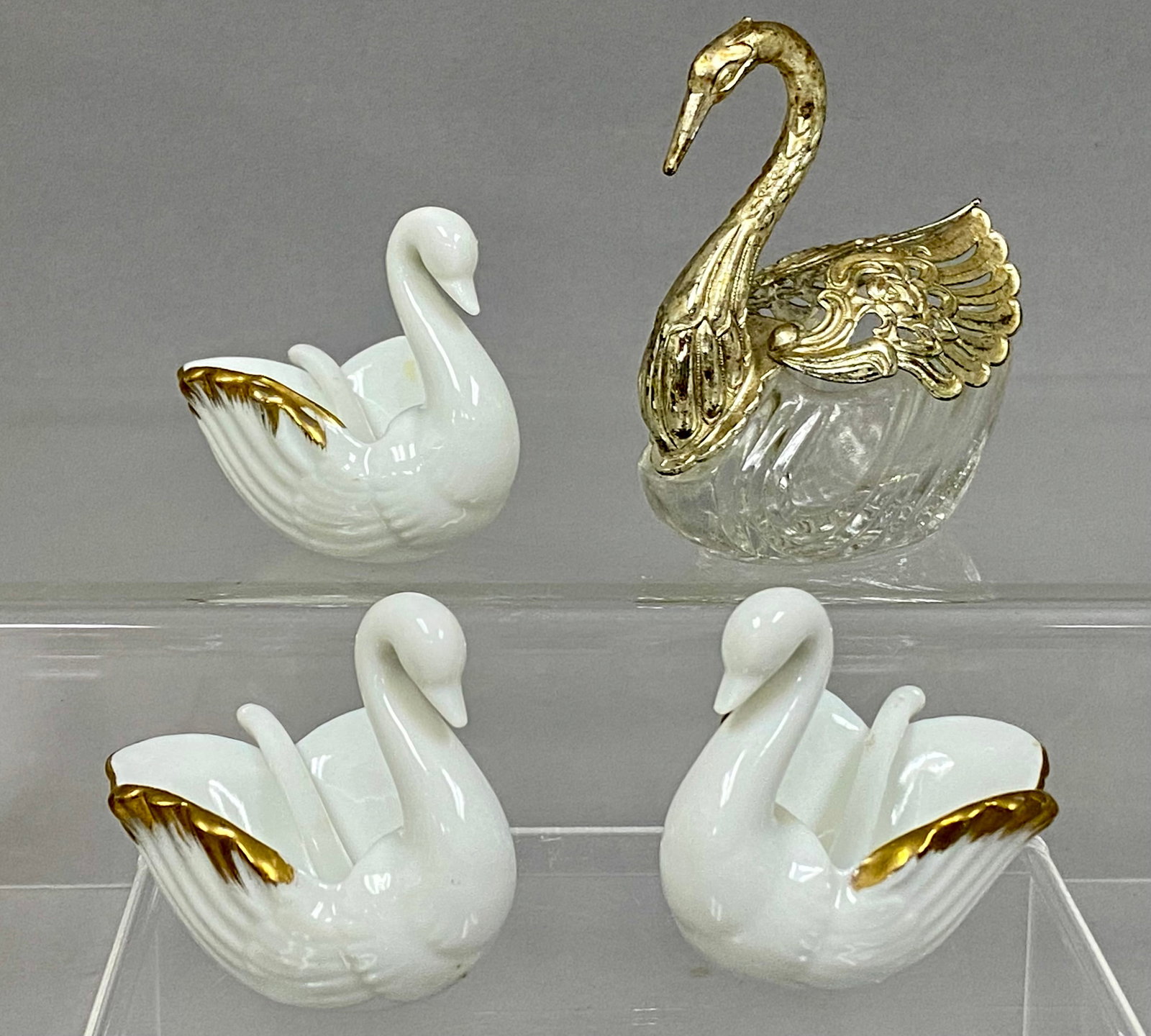 A Collection of Swan Salt Cellars: This group features three porcelain salt cellars by Royal Kendall and a single mixed-media swan-form dish. The porcelain pieces are decorated with gilt wing tips and include matching spoons, with each
