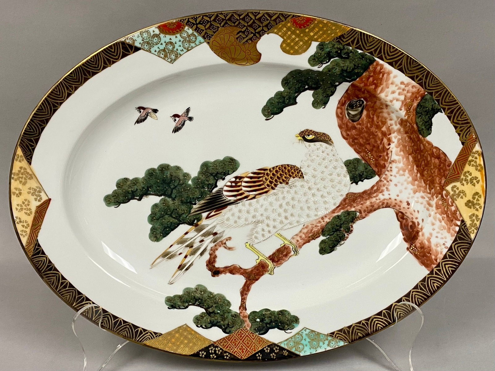 Antique Japanese Kaga Kutani Porcelain Charger: Japanese Kutani porcelain Hawk & Pine Tree platter measures 16" long by 12" wide. The center features a highly detailed, hand-painted motif of a hawk perched on a stylized pine tree (Taka ni matsu), a