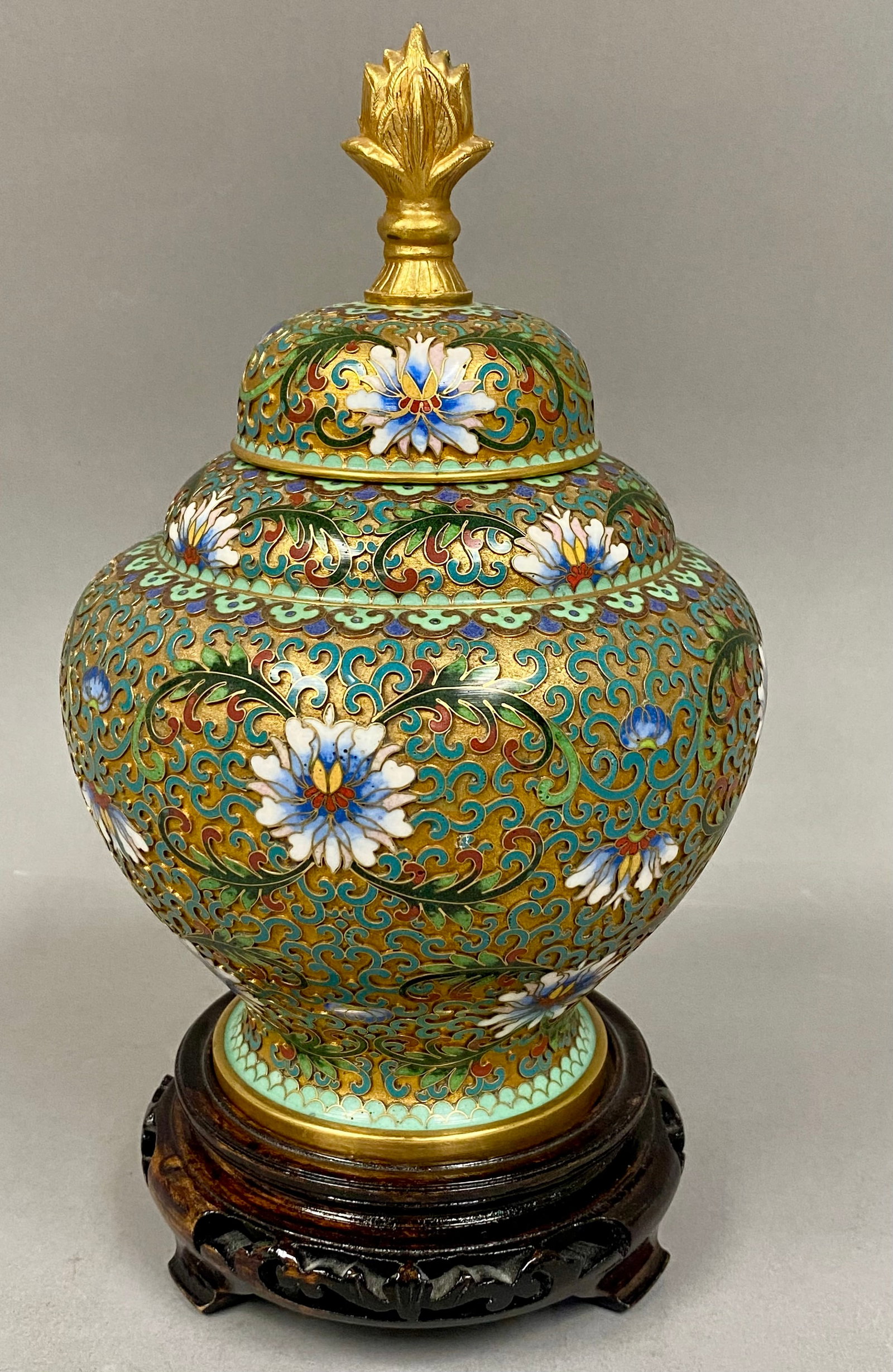 Chinese Cloisonne Enamel Jar and Cover on Carved Wood Stand: A Chinese cloisonne enamel jar of baluster form with a matching domed cover, presented on a dark-stained carved wooden stand. The exterior is decorated with large multi-petaled lotus blossoms rendered