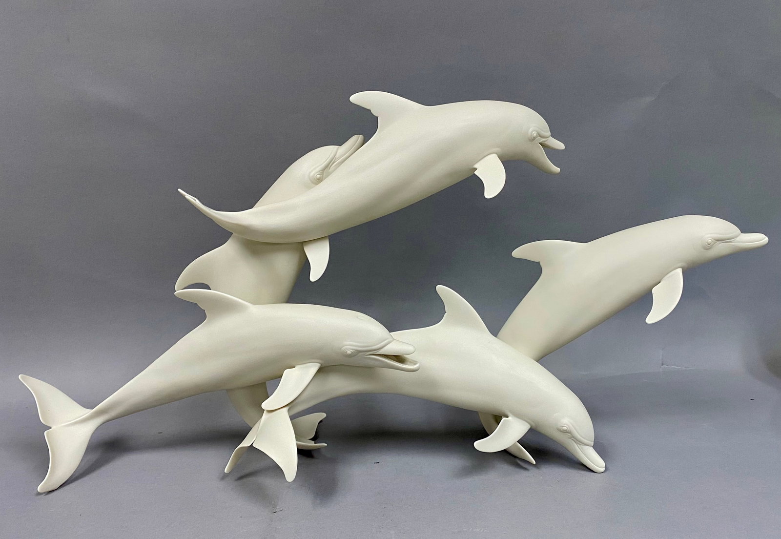 Limited Edition Bisque Porcelain Pod of Dolphins by Gunther Granget: A large bisque porcelain sculpture depicting a group of dolphins leaping in a dynamic, circular arrangement. The piece is constructed from unglazed, matte white porcelain, capturing anatomical details