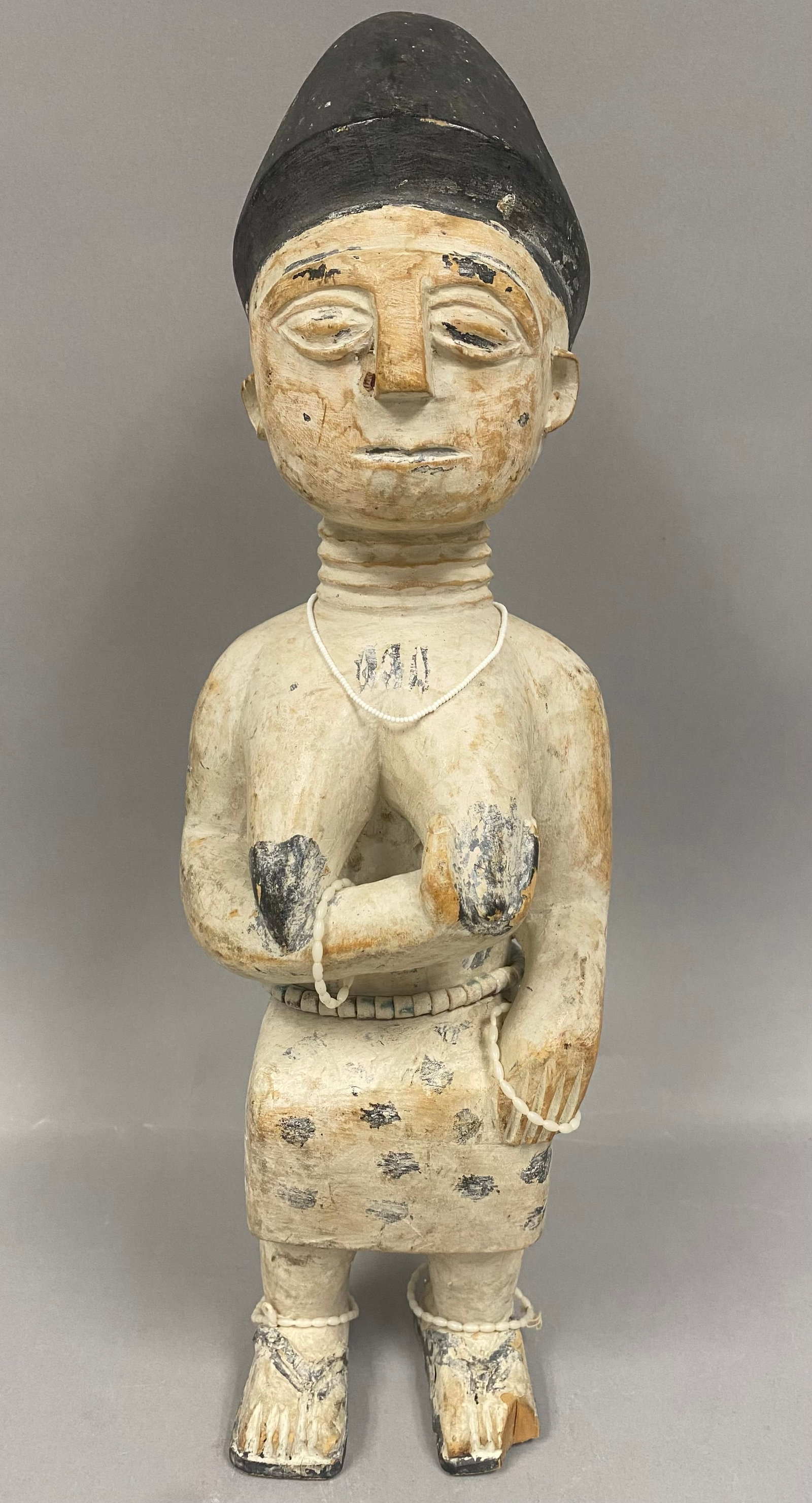 West African Wooden Standing Female Figure: The hand-carved wooden figure is covered in a thick layer of white kaolin pigment, a material traditionally used in ritual contexts to represent spiritual purity or connection to the ancestor world. T