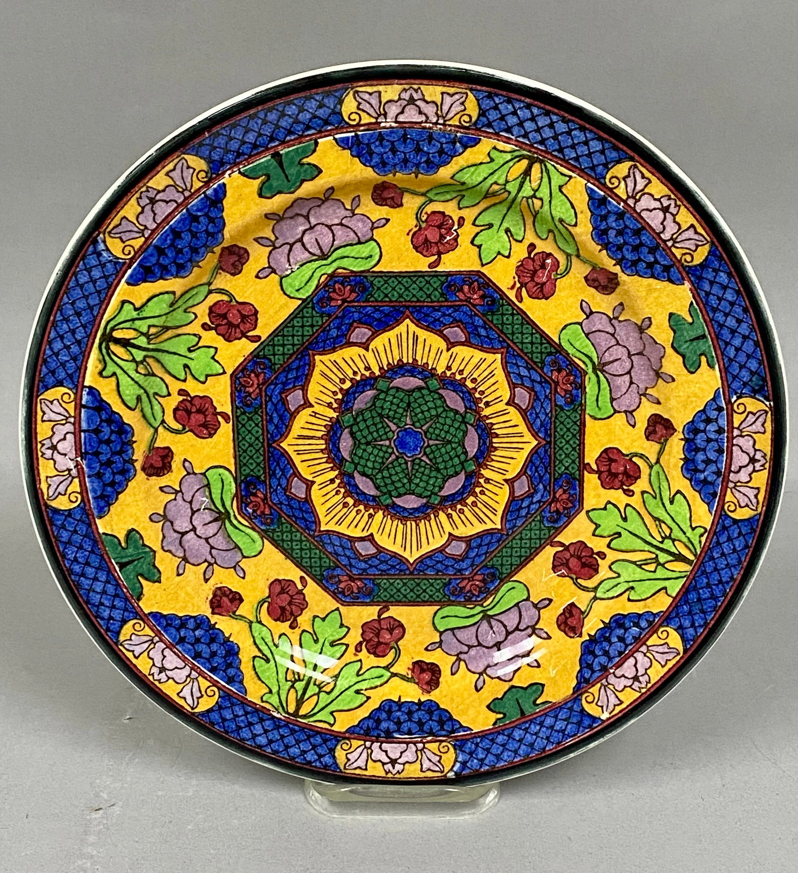 1933 Royal Doulton Rack Plate Pattern # D4550: Produced in England in 1933. The design features a colorful geometric floral medallion in yellow, blue, green, and red, finished with a patterned border. The back features the standard Royal Doulton