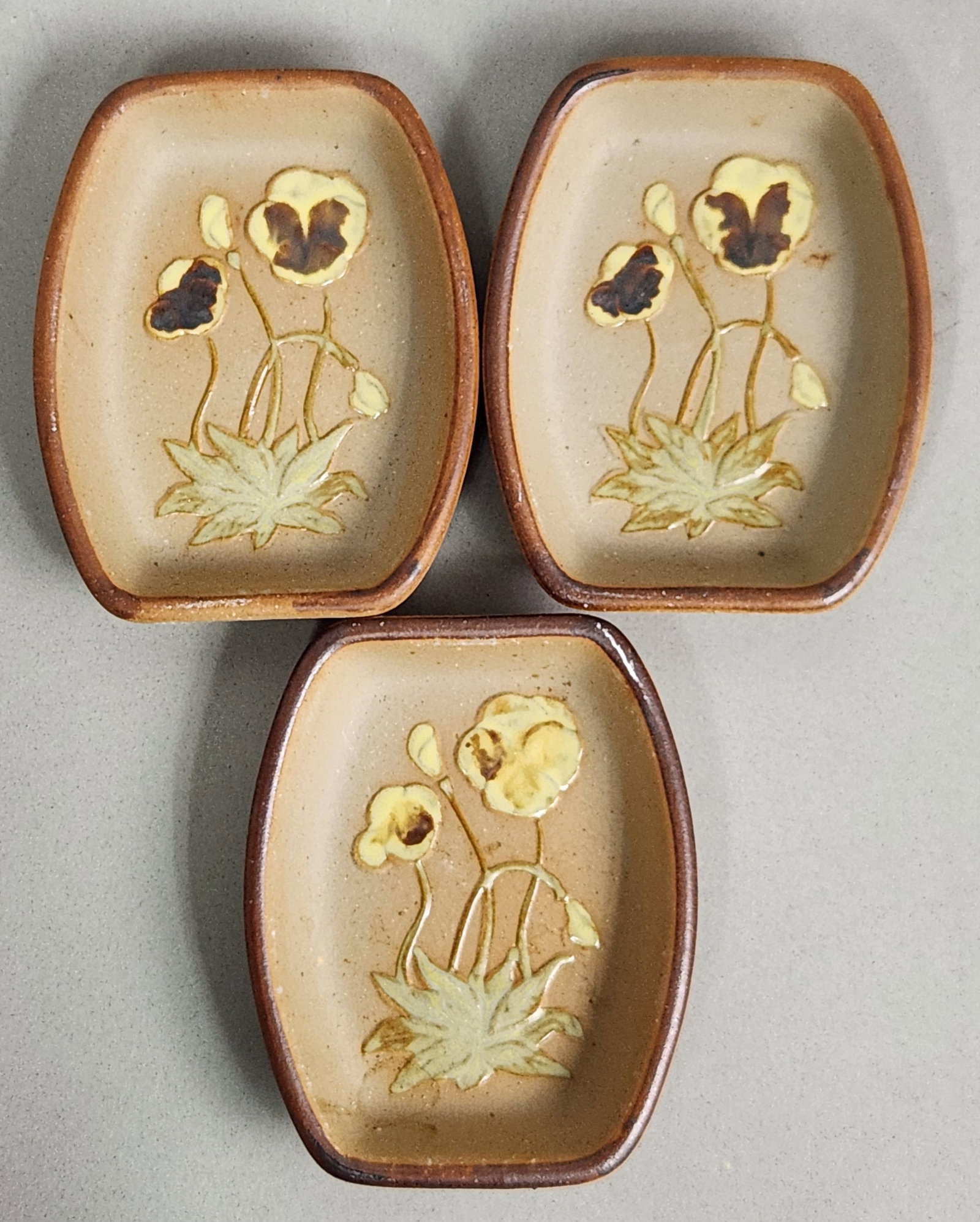 Trio of Stoneware Pansy Dishes: A trio of small rectangular stoneware dishes featuring a sprigged botanical motif of pansies in yellow and brown glazes. Dimensions: 4 x 3 inches (each). Excellent condition with no chips, cracks, or