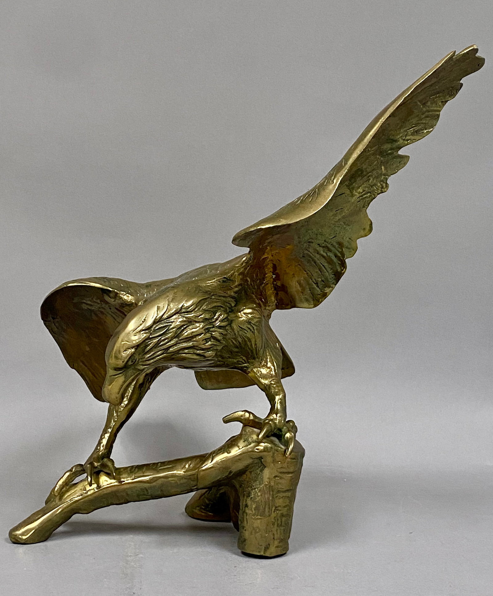 Large Vintage Brass Eagle Sculpture: A large-scale decorative sculpture of an eagle depicted with upward-swept wings perched upon a textured tree branch. The figure is constructed of cast brass with a polished finish and retains an origi
