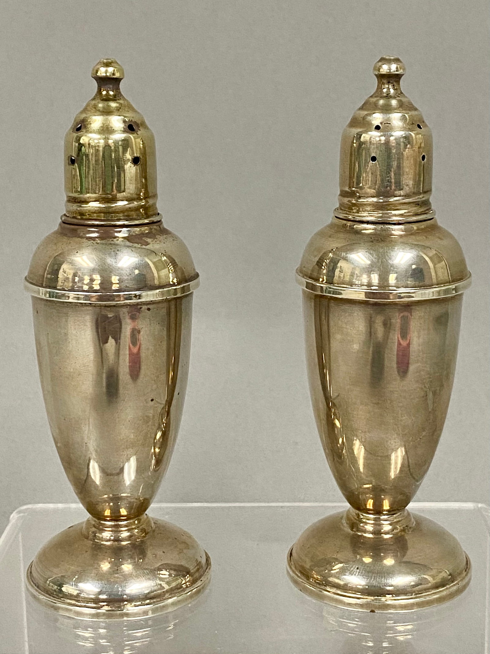 Reed & Barton Sterling Silver Shakers: A pair of Reed & Barton sterling silver salt and pepper shakers in the Pilgrim pattern, model number 40. The shakers are designed in a classic urn form with circular pedestal bases and screw-on domed 