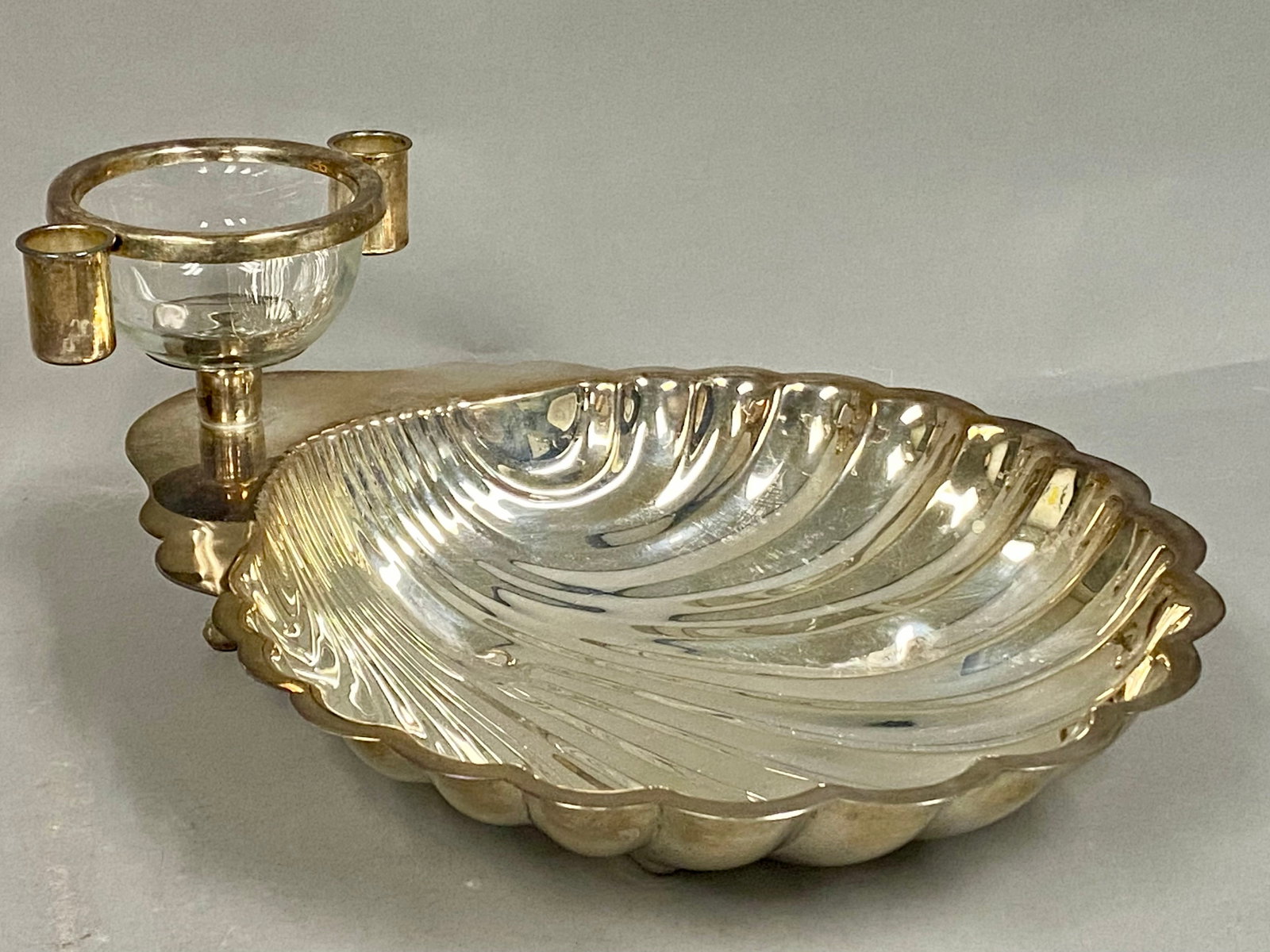Sheridan Silverplated Shell Seafood Server: A Sheridan silver-plated seafood server featuring a fluted scallop shell base supported by three feet. An elevated superstructure at the rear holds a central removable clear glass bowl and two