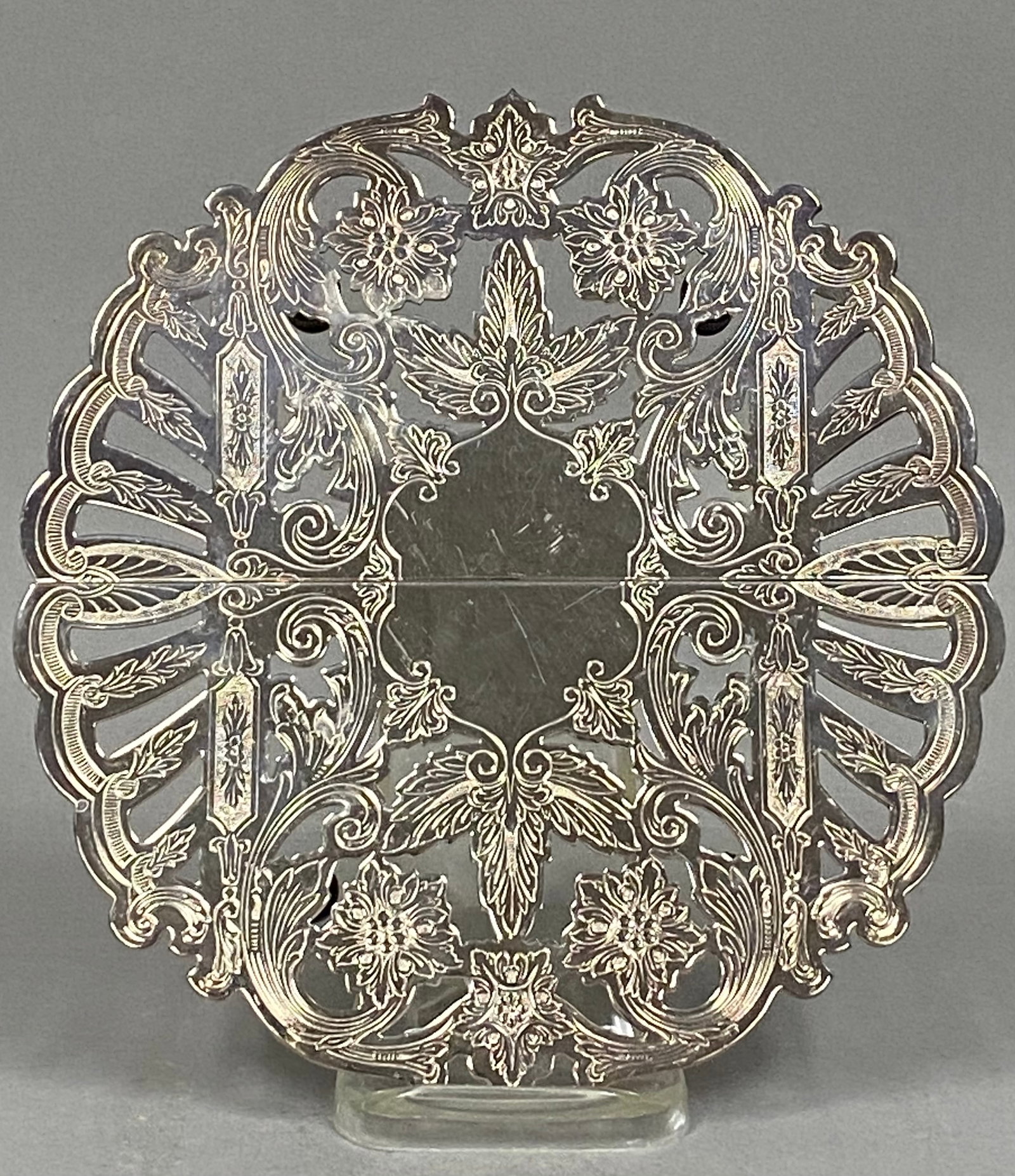 Wallace Silverplate Expandable Floral Trivet: This Wallace Silversmiths expandable silverplate trivet features an ornate pierced design of scrollwork, acanthus leaves, and floral motifs. The circular body adjusts via a sliding mechanism and