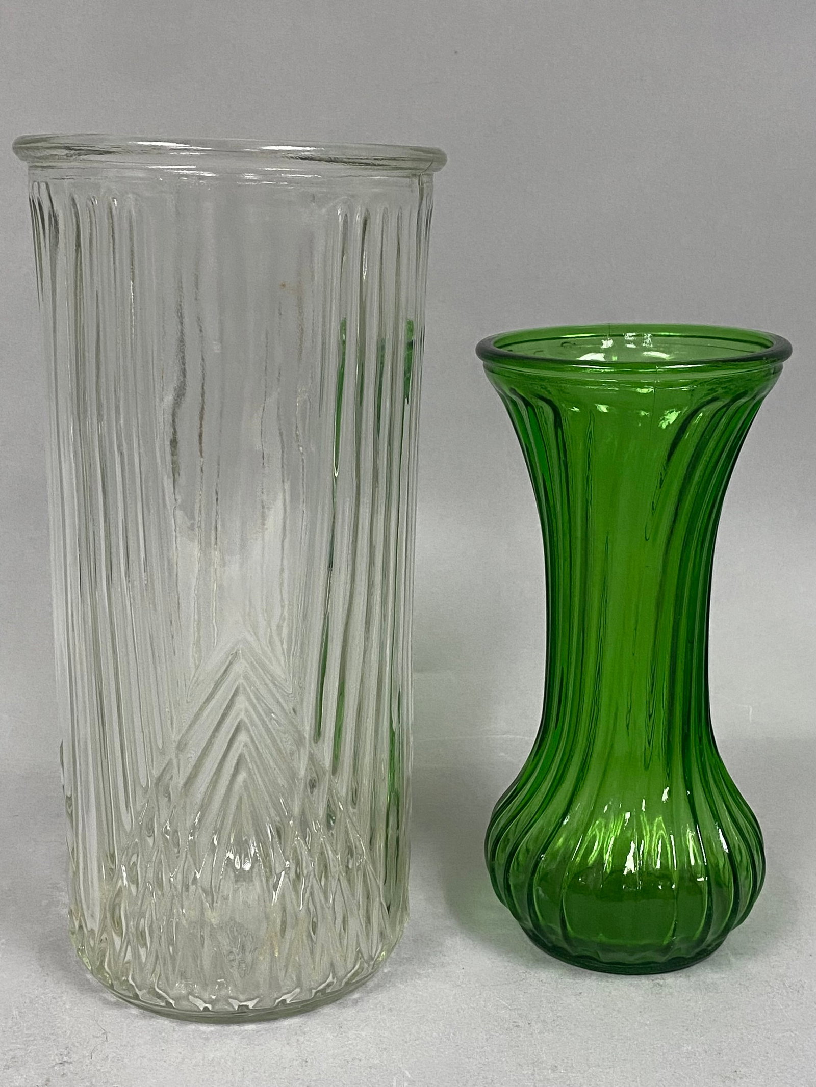 2 Hoosier Pressed Glass Vases: This lot features two vintage pressed glass vases by Hoosier Glass, including a clear cylindrical vase and an emerald green fluted vase. The clear vessel, model 4101, displays vertical ribbing over a