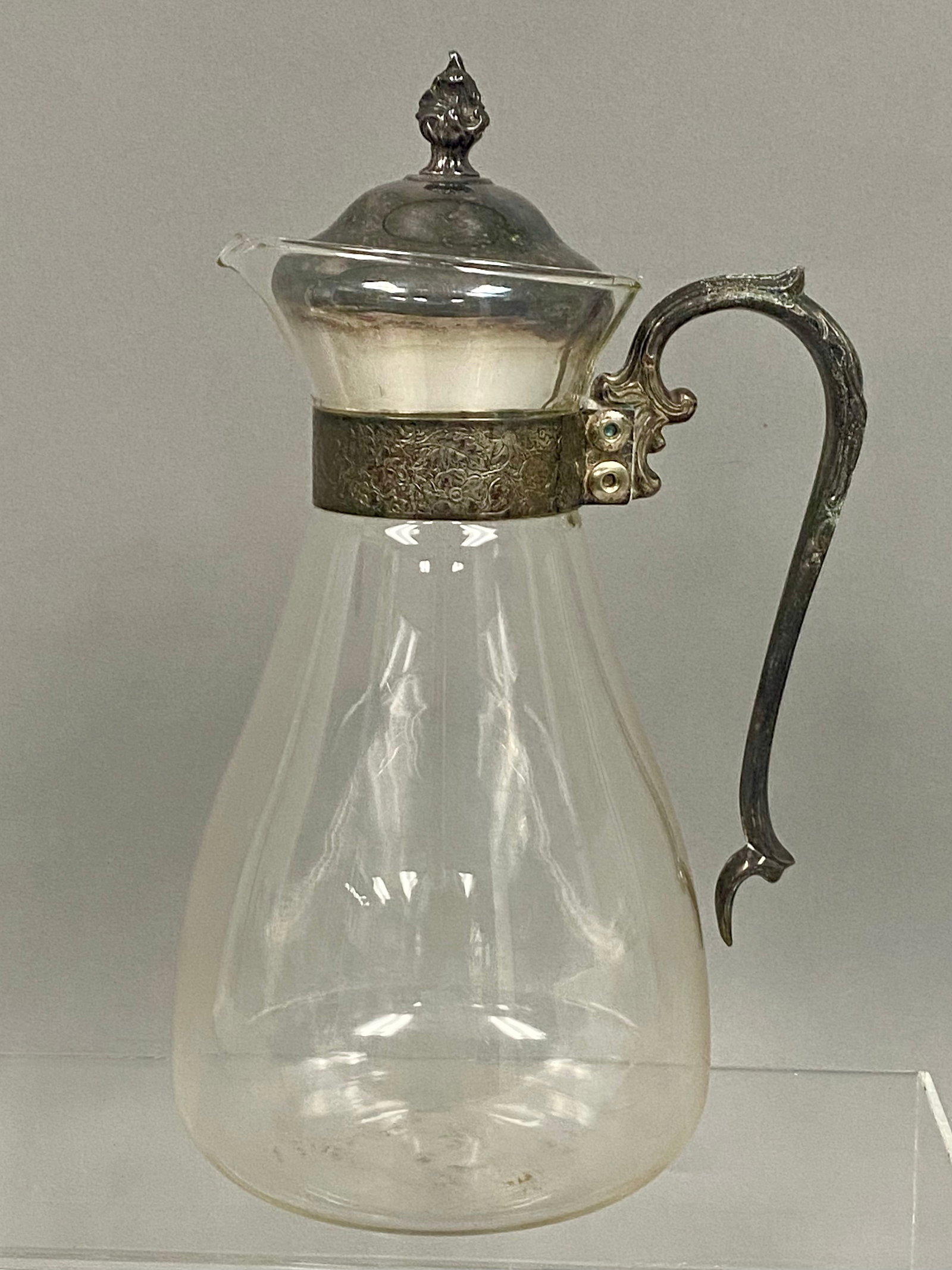Victorian Silver-Plated Glass Claret Jug: This Victorian-style claret jug features a clear glass tapering body fitted with silver-plated mounts. The metalwork consists of a wide collar with floral repoussÄ‚Â© decoration