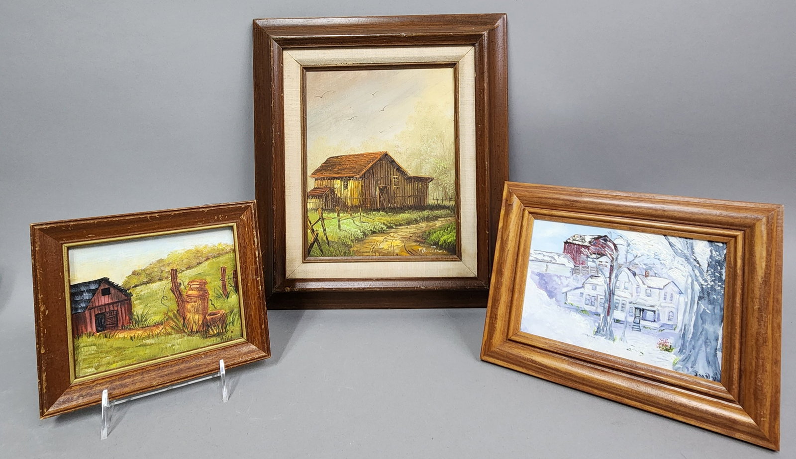 Three Rural Landscapes Oil Paintings: Three rural landscape paintings executed in oil on canvas and board. The largest work depicts a weathered wooden barn alongside a dirt path with birds in flight, signed T. Burton in the lower right.