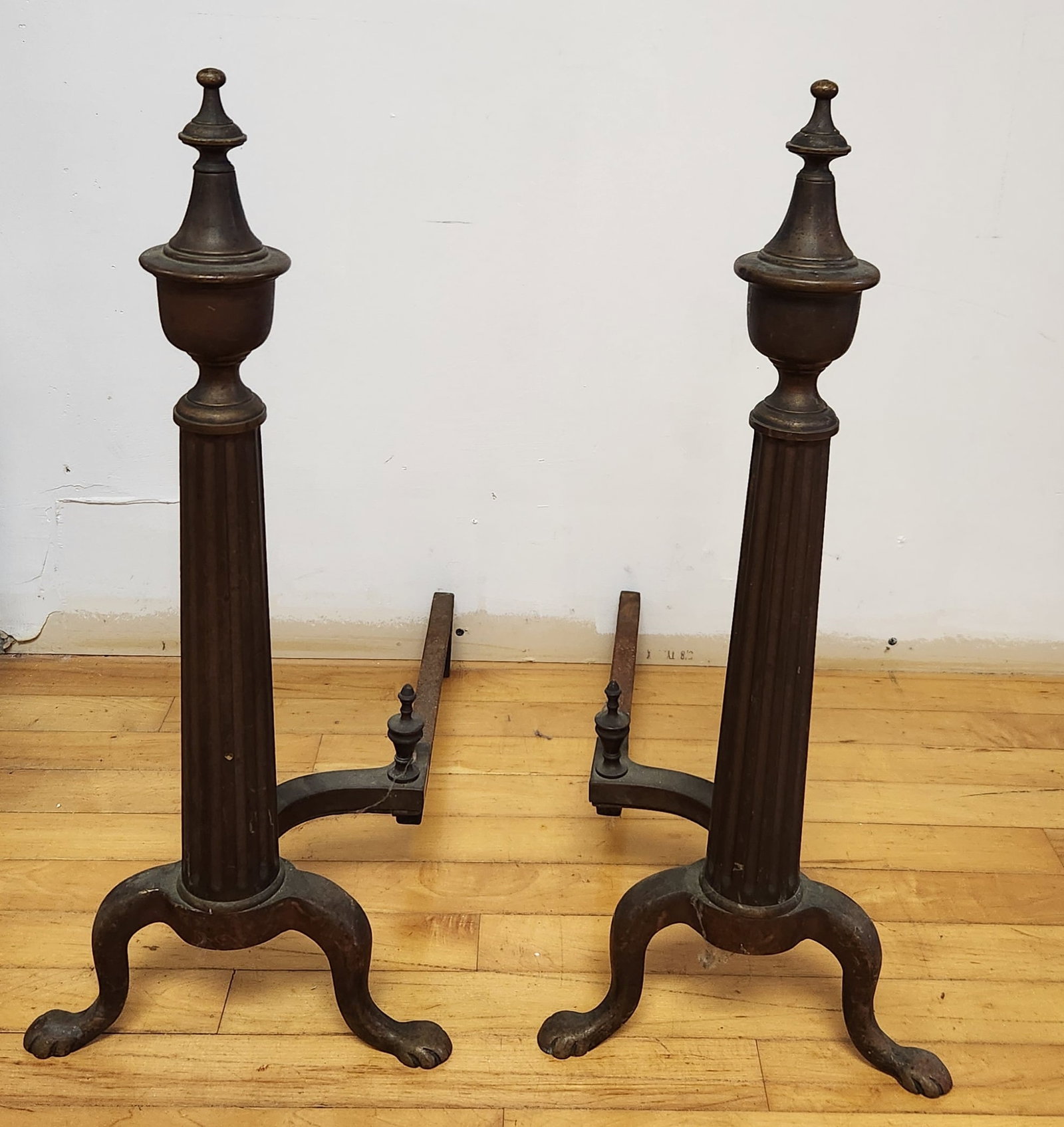 Pair Classical Brass Andirons: This pair of tall Neoclassical-style andirons features fluted columnar shafts surmounted by tiered urn-form finials with ball tips. Height: 24.5 inches. The brass components show heavy oxidation and